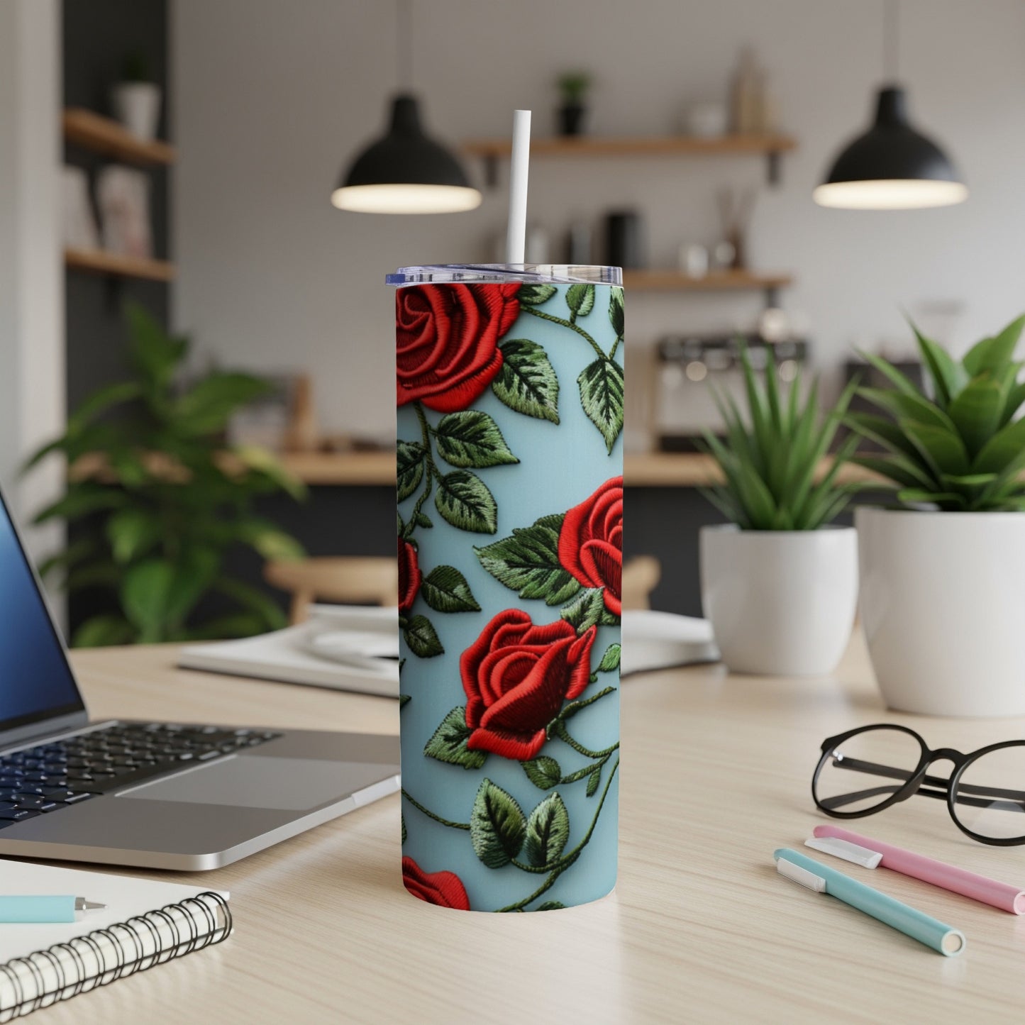 Light blue tumbler with red roses and green leaves design, on a desk.