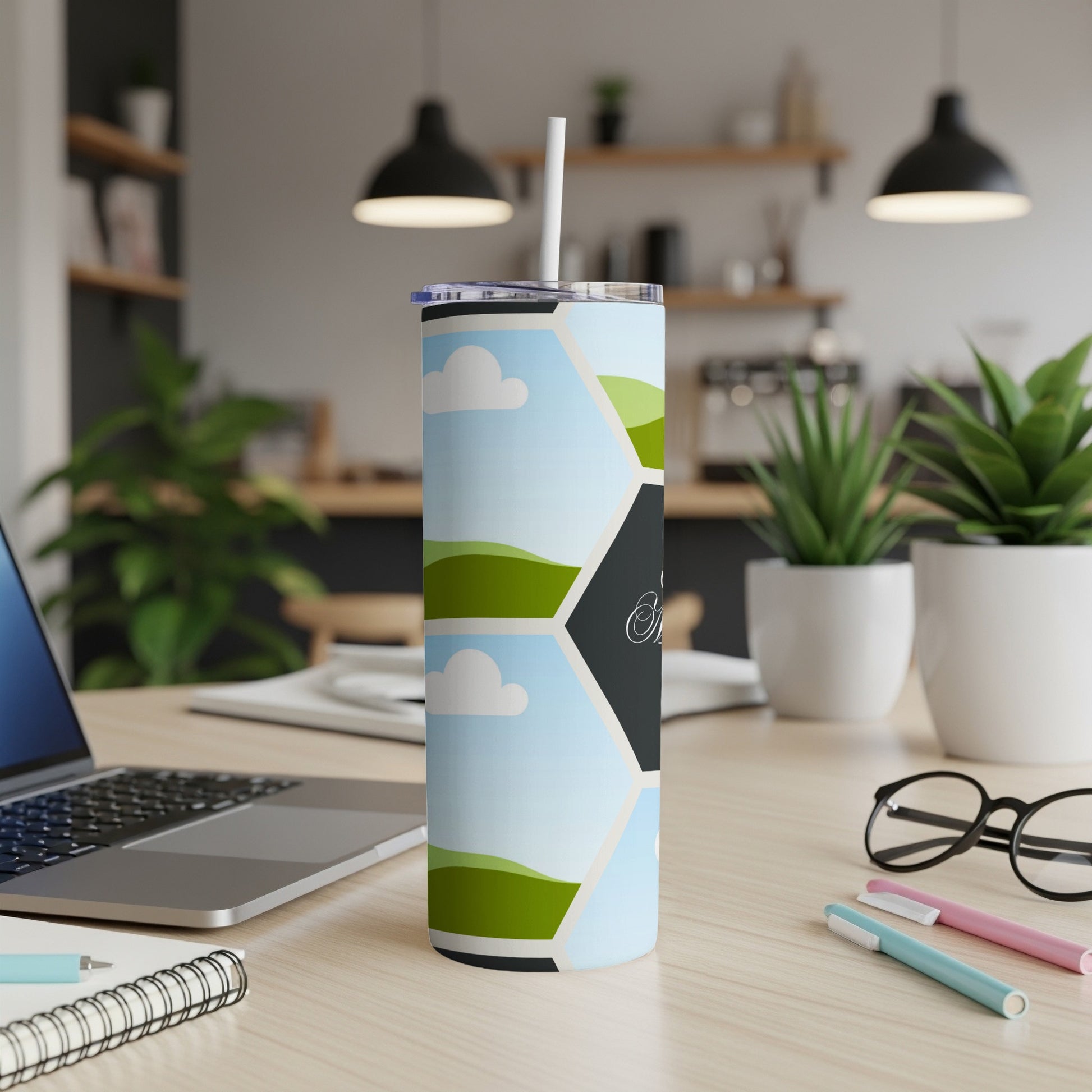Tumbler with a hexagonal landscape design and a straw, on a desk.