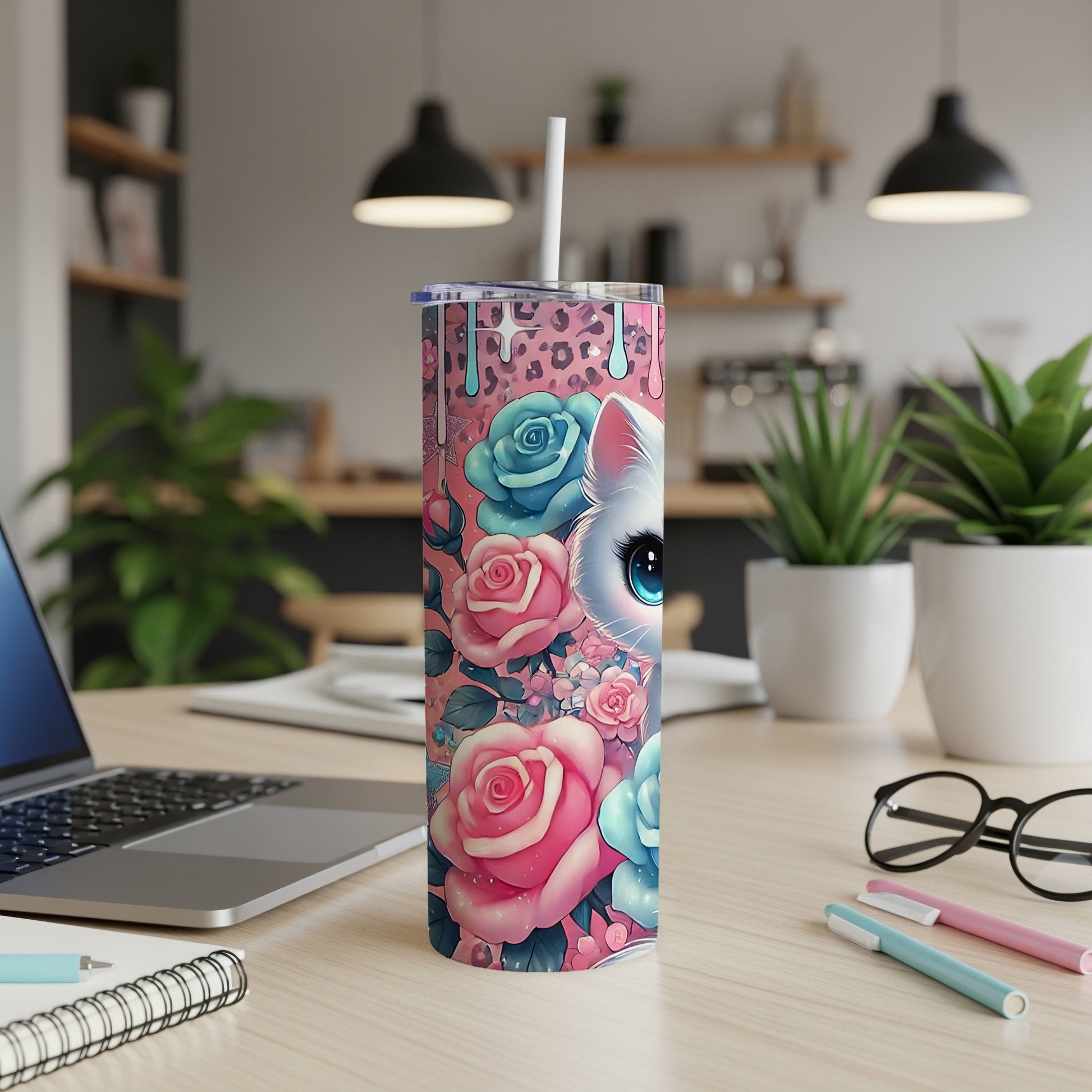 Tumbler with white cat and pink and blue roses, on a desk.