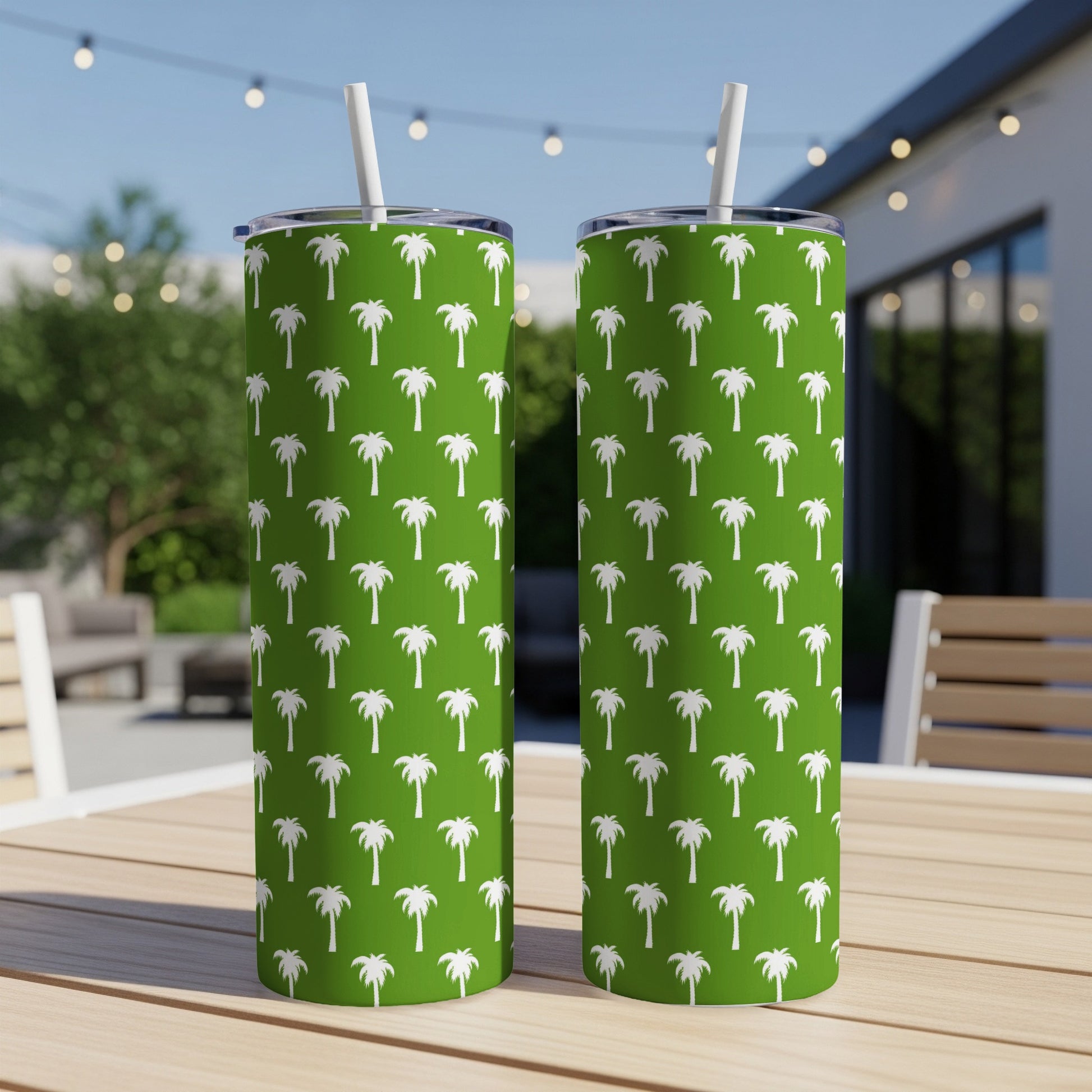 Two green tumblers with white palm tree pattern and straws on a table.