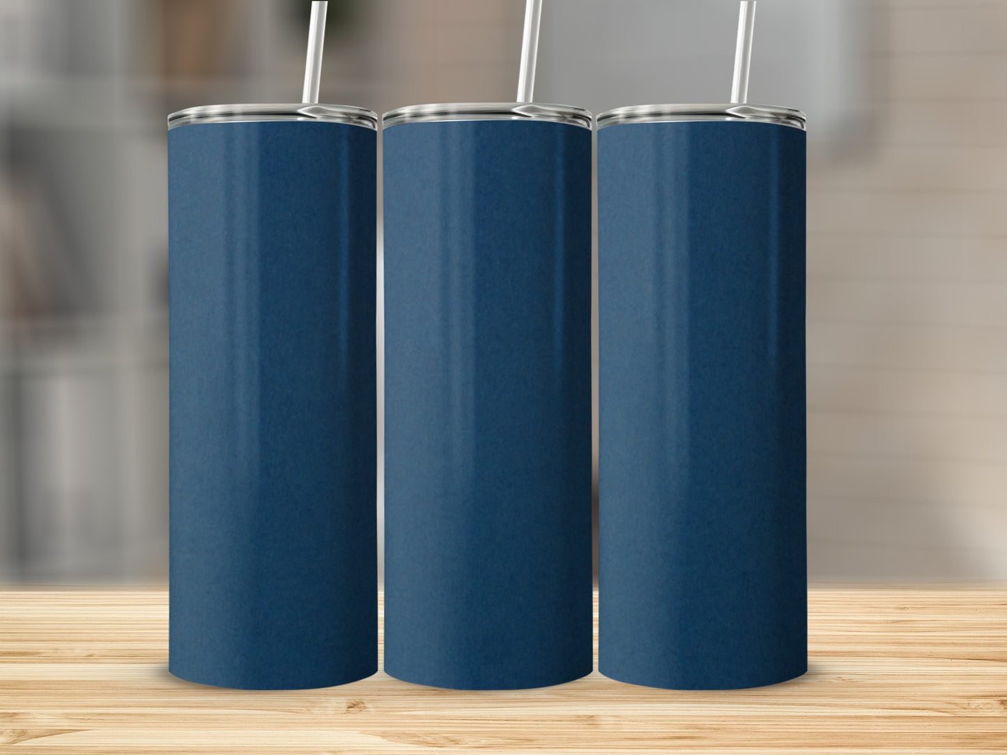 Three plain navy blue tumblers with white straws stand on a wooden surface.