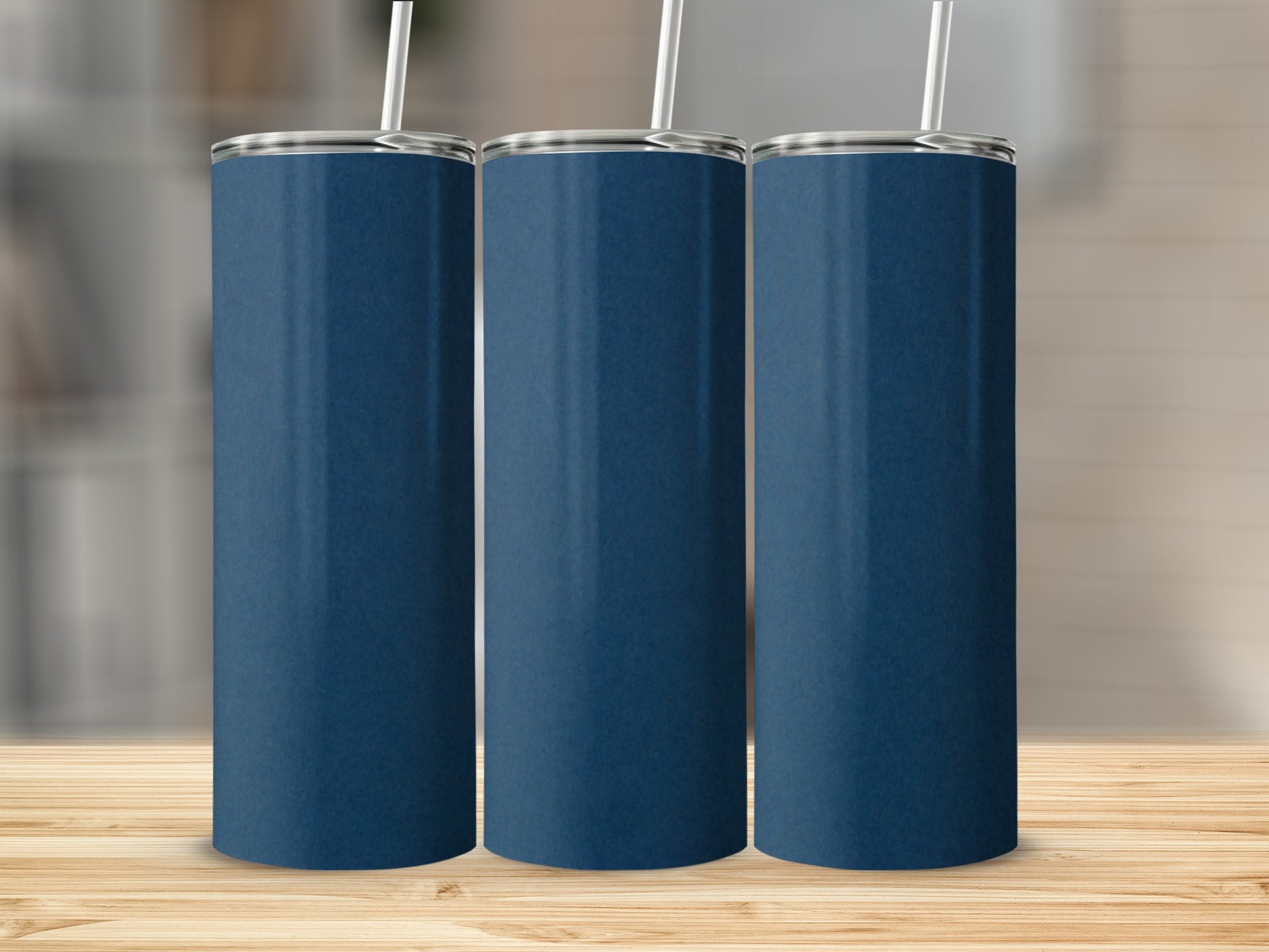 Three plain navy blue tumblers with white straws stand on a wooden surface.