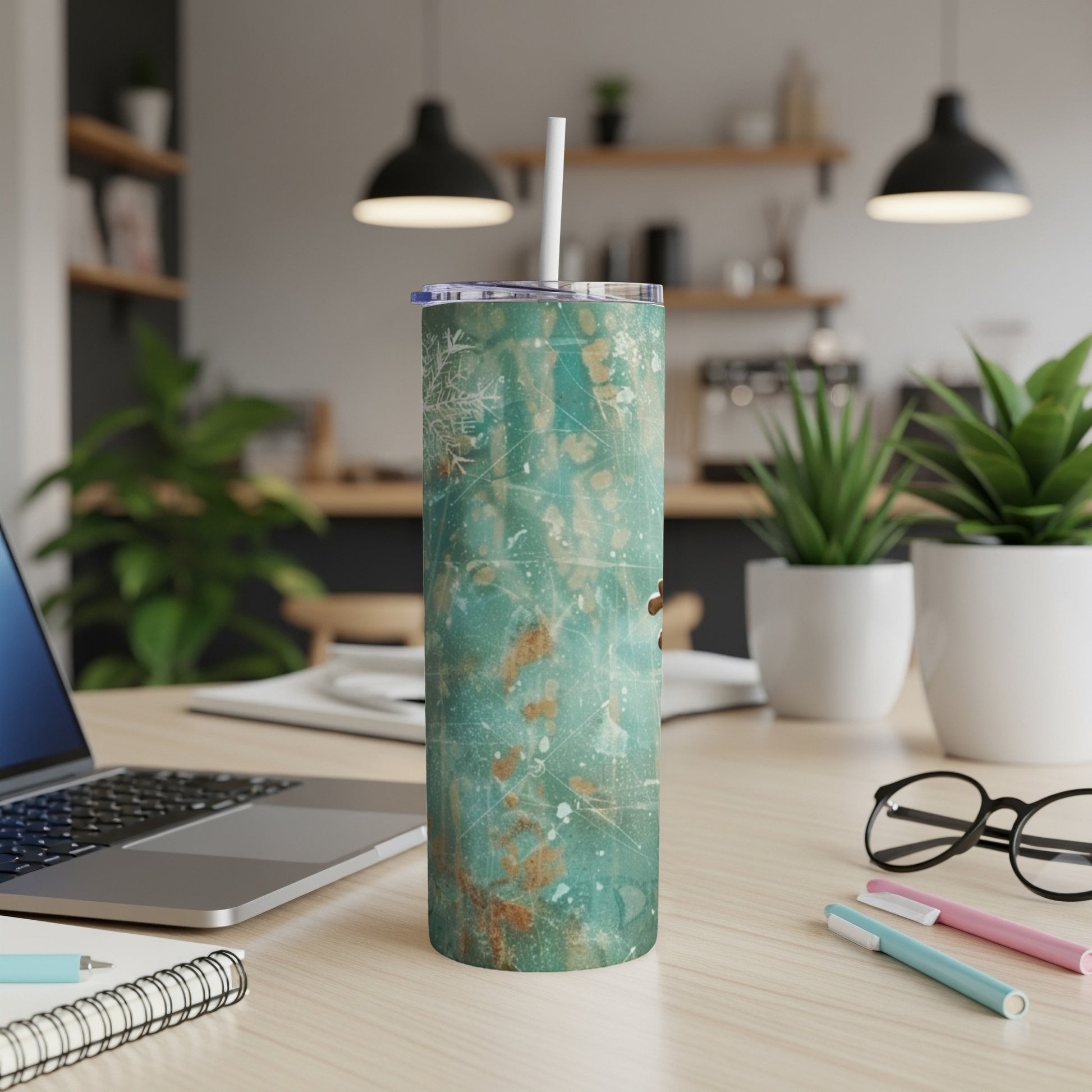 Turquoise and copper abstract art design skinny tumbler with straw on desk.