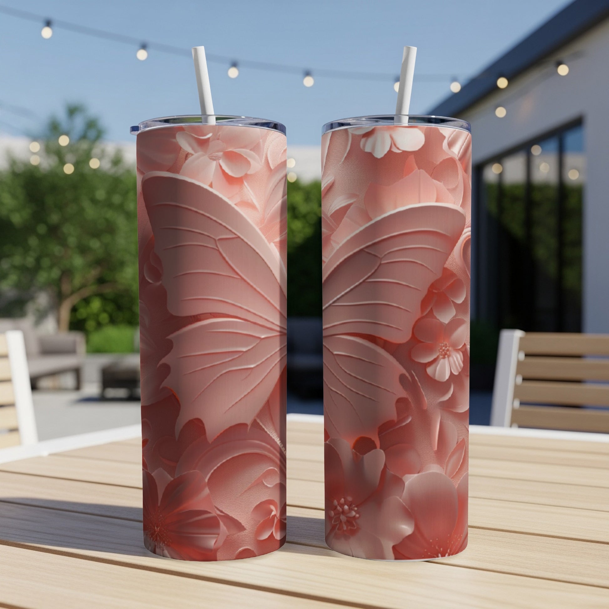 Two pink butterfly and floral pattern tumblers with straws on a table.