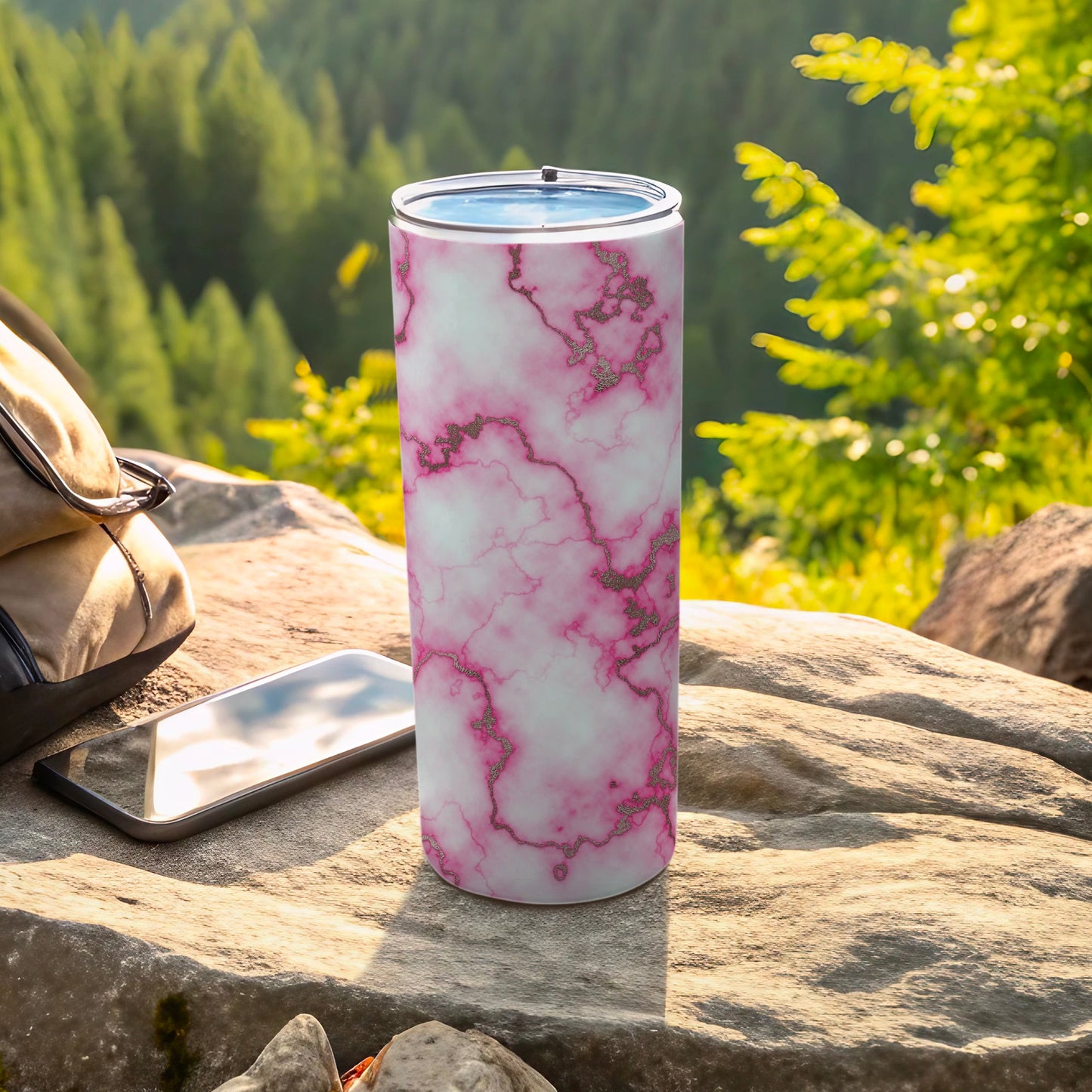 Pink and gold marble tumbler with phone and backpack on rock.