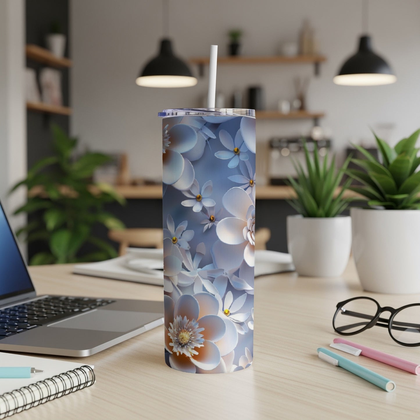 Floral patterned tumbler with straw on a desk with a laptop and pens.
