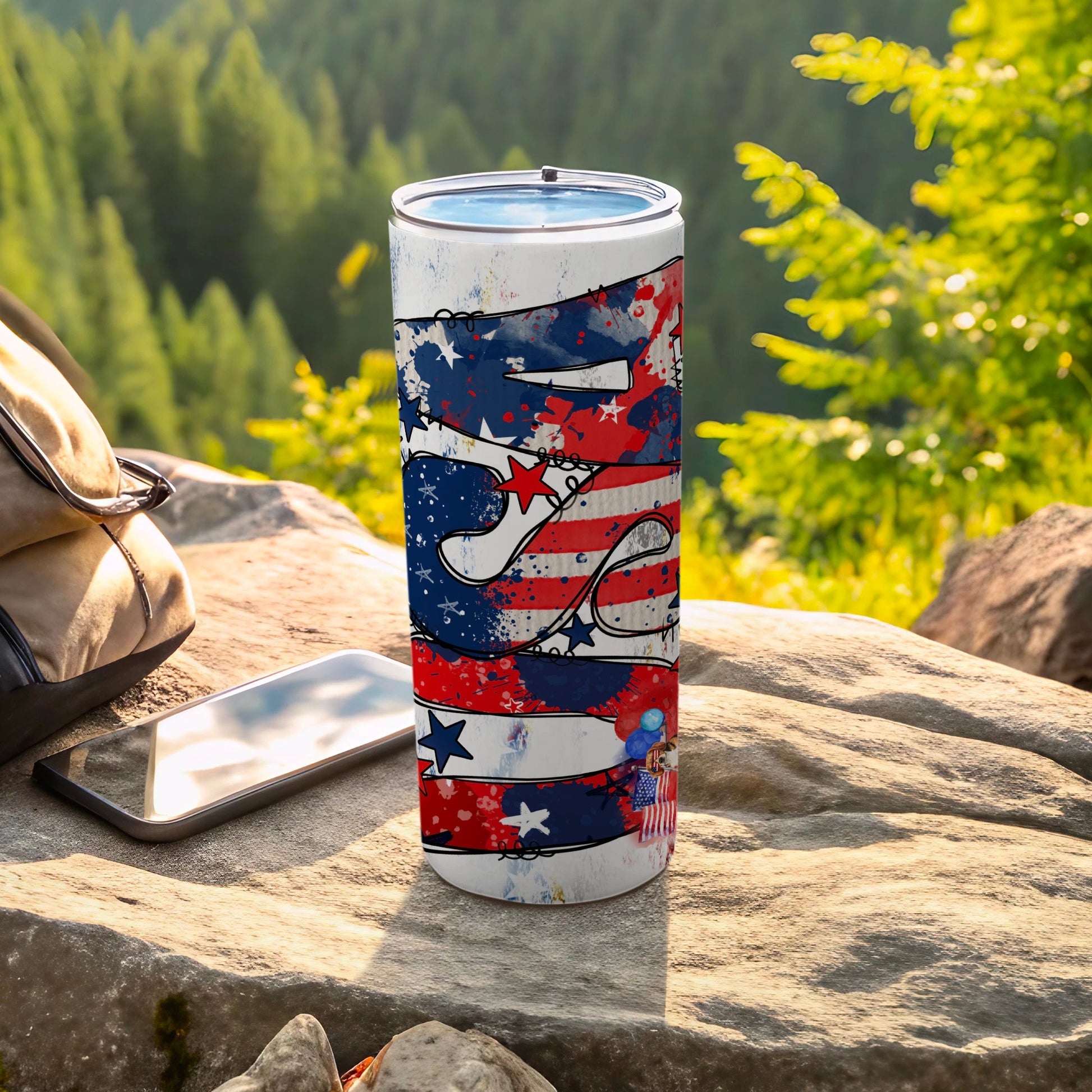 Patriotic tumbler with stars, stripes, and fireworks on a rocky surface.