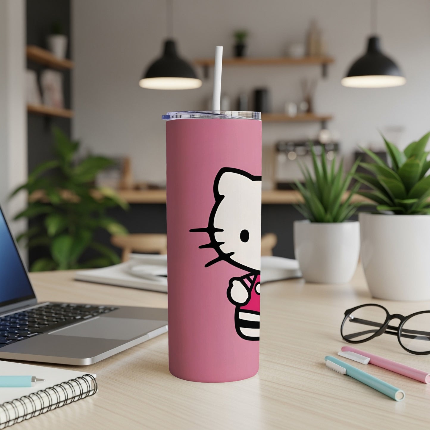 Pink Hello Kitty tumbler with straw on desk next to laptop and pens.