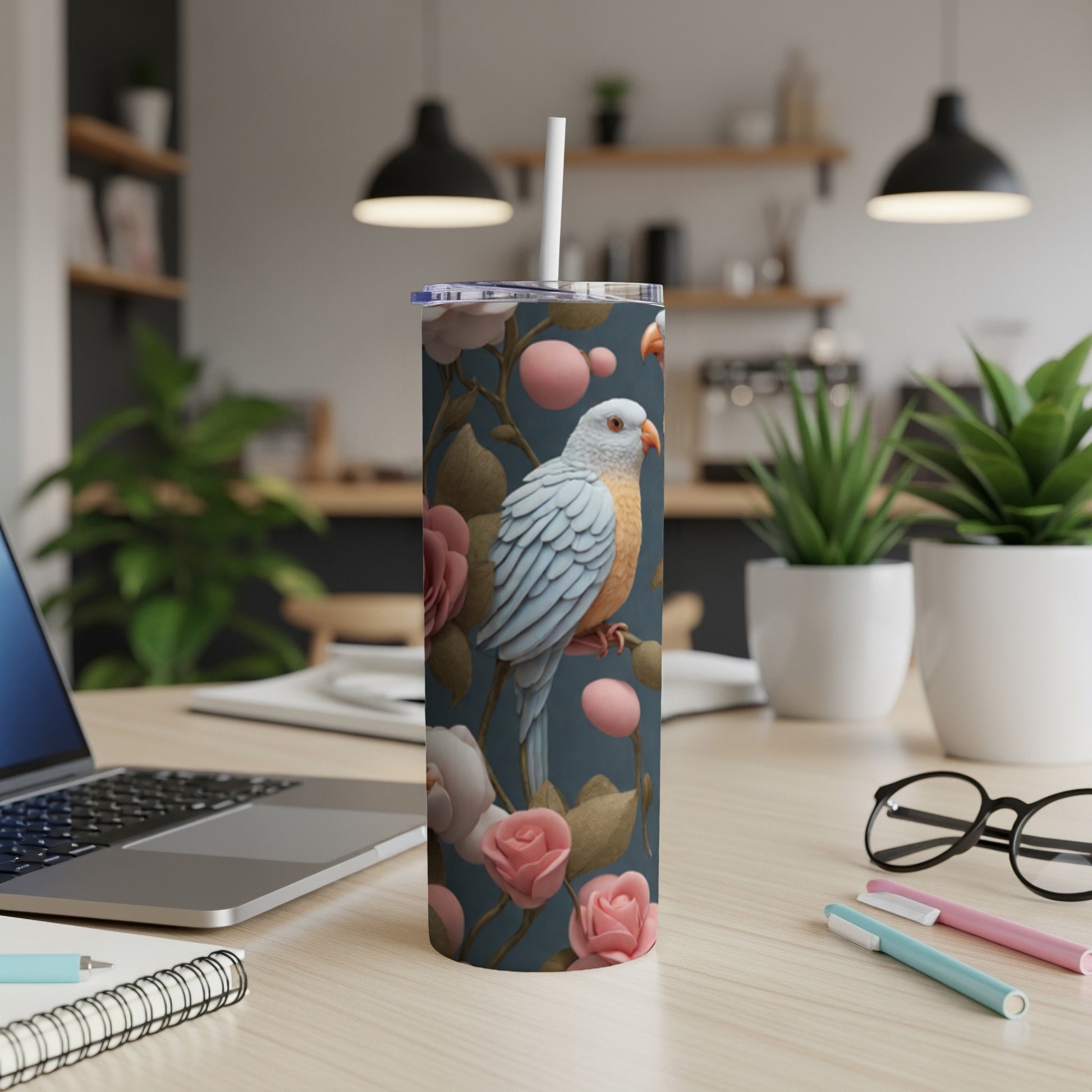 Blue tumbler with parrot and pink roses, on a desk with laptop.