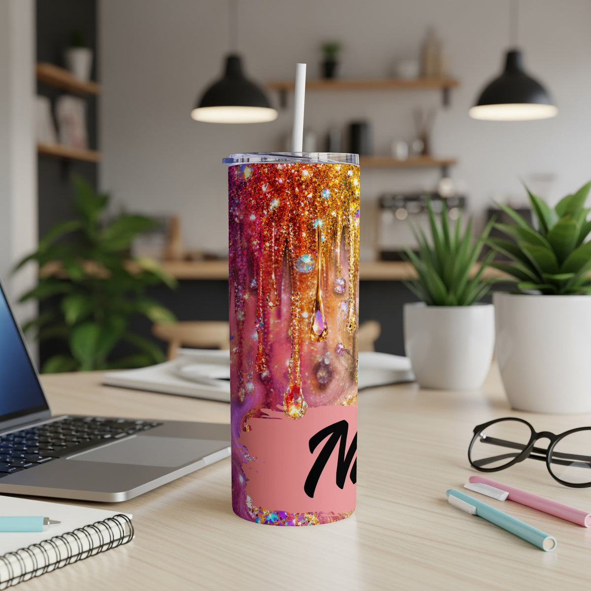 Tumbler with dripping glitter design and initial "M" on a desk.