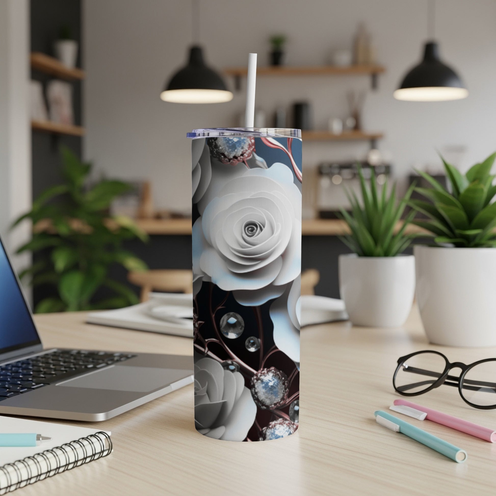 White roses and clear gems adorn a skinny tumbler on a desk.