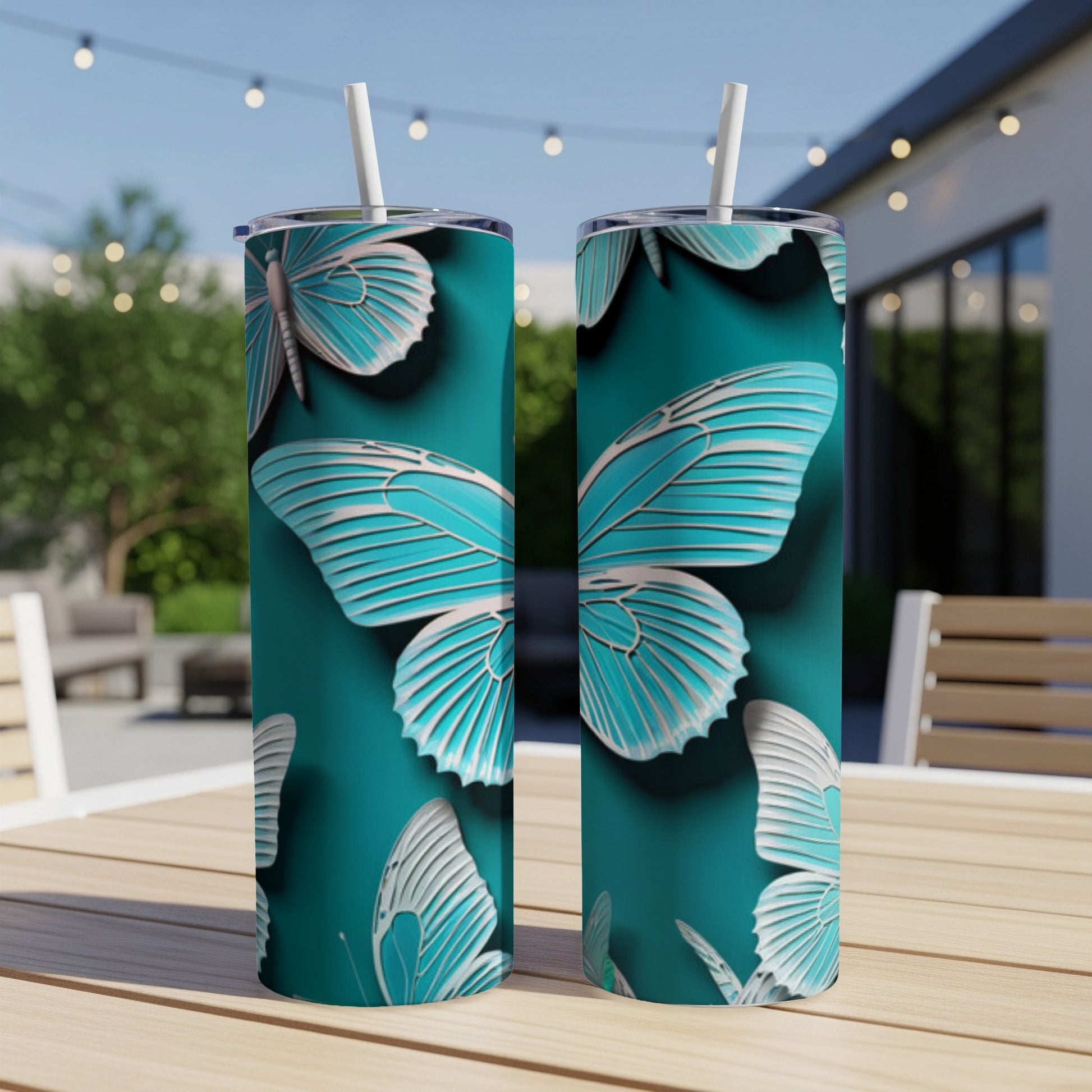 Two teal tumblers with a blue butterfly pattern sit on a table outdoors.