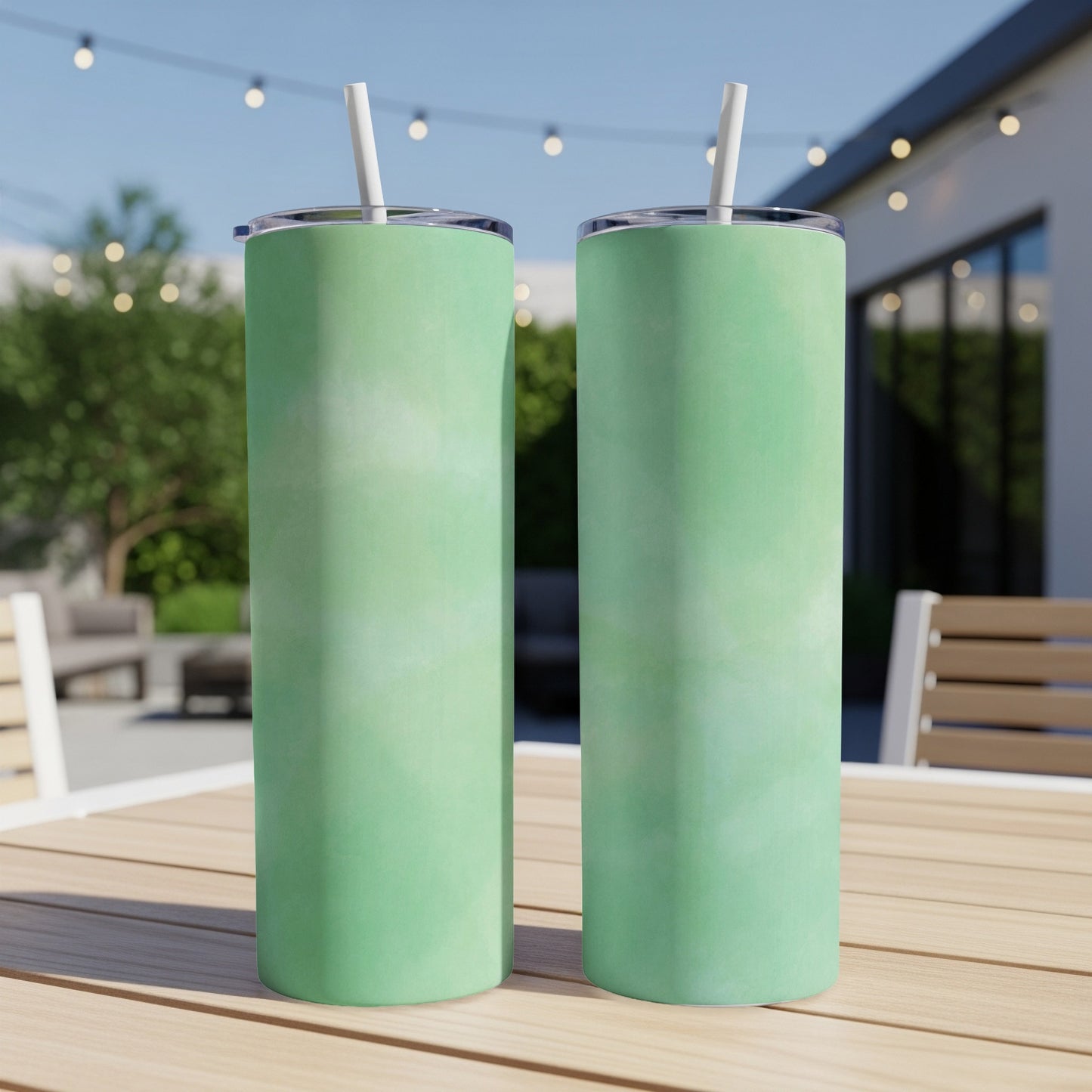 Two green tumblers with straws sit on a wooden table outdoors.