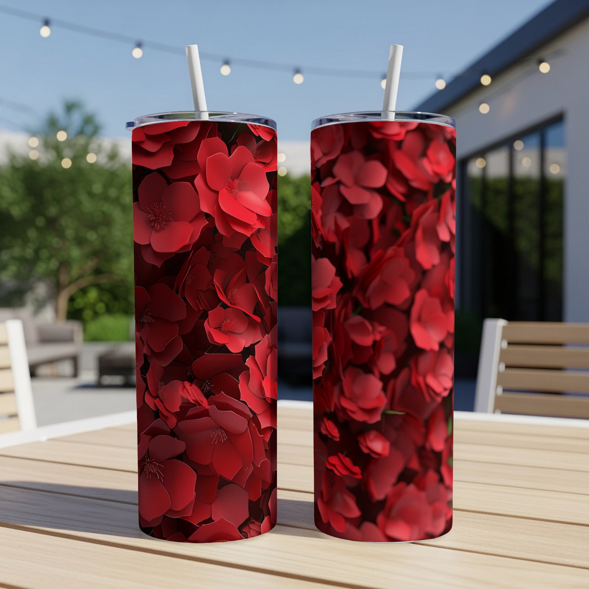 Two red floral tumblers with straws on a wooden table outdoors.