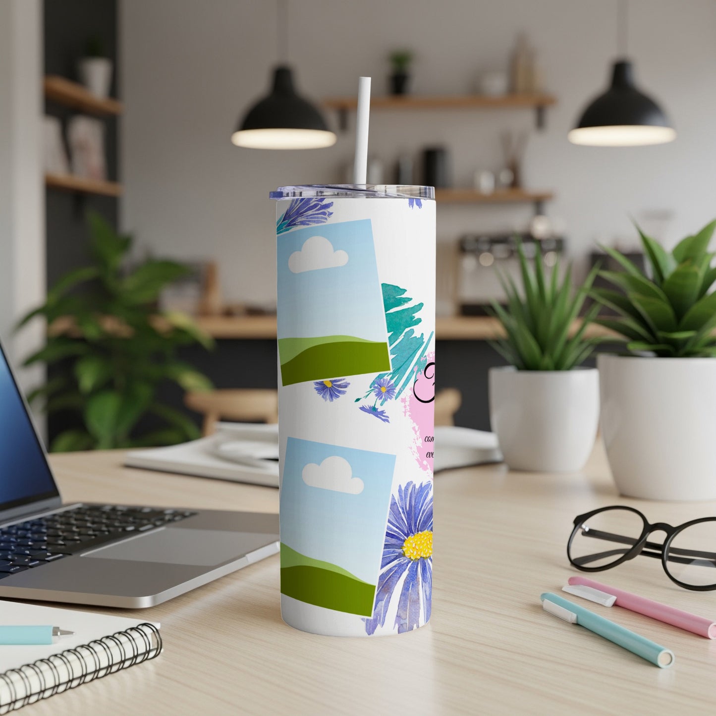 Tumbler with floral design and photo frames on a desk with laptop and glasses.