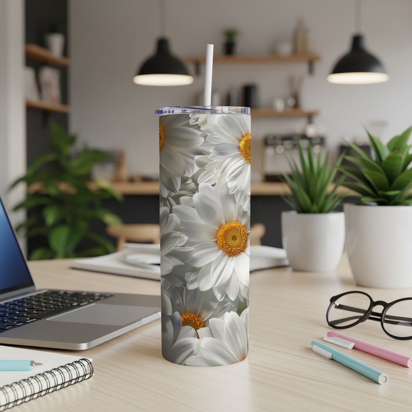 White daisies with yellow centers wrap around a white tumbler on a desk.