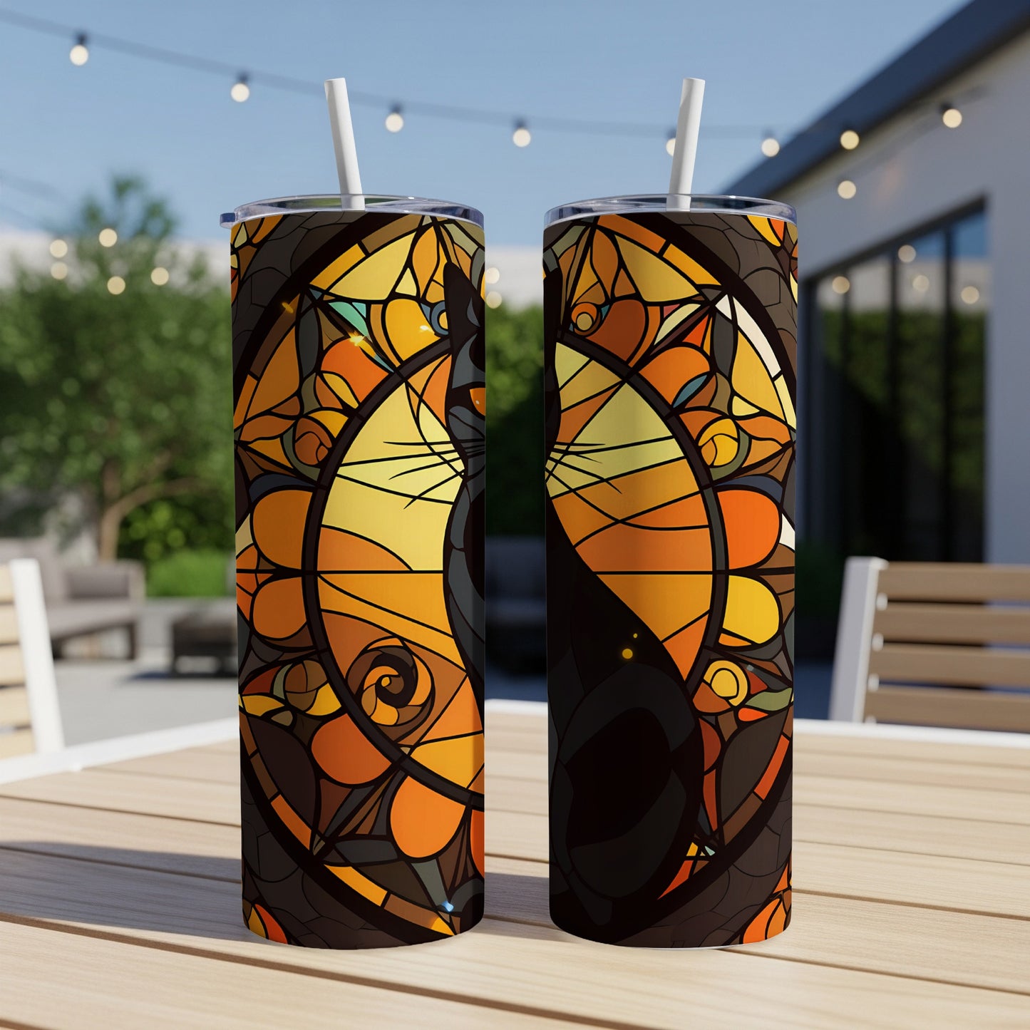 Two tumblers with stained glass cat designs sit on a patio table.