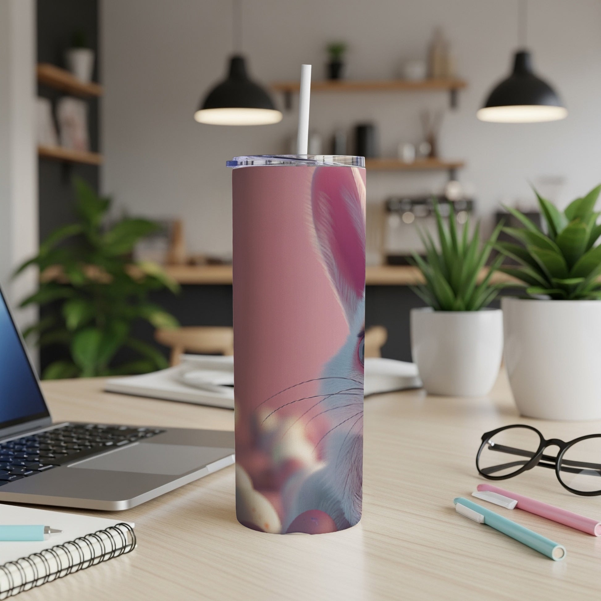 Pink tumbler with Easter bunny design on a desk with a laptop.