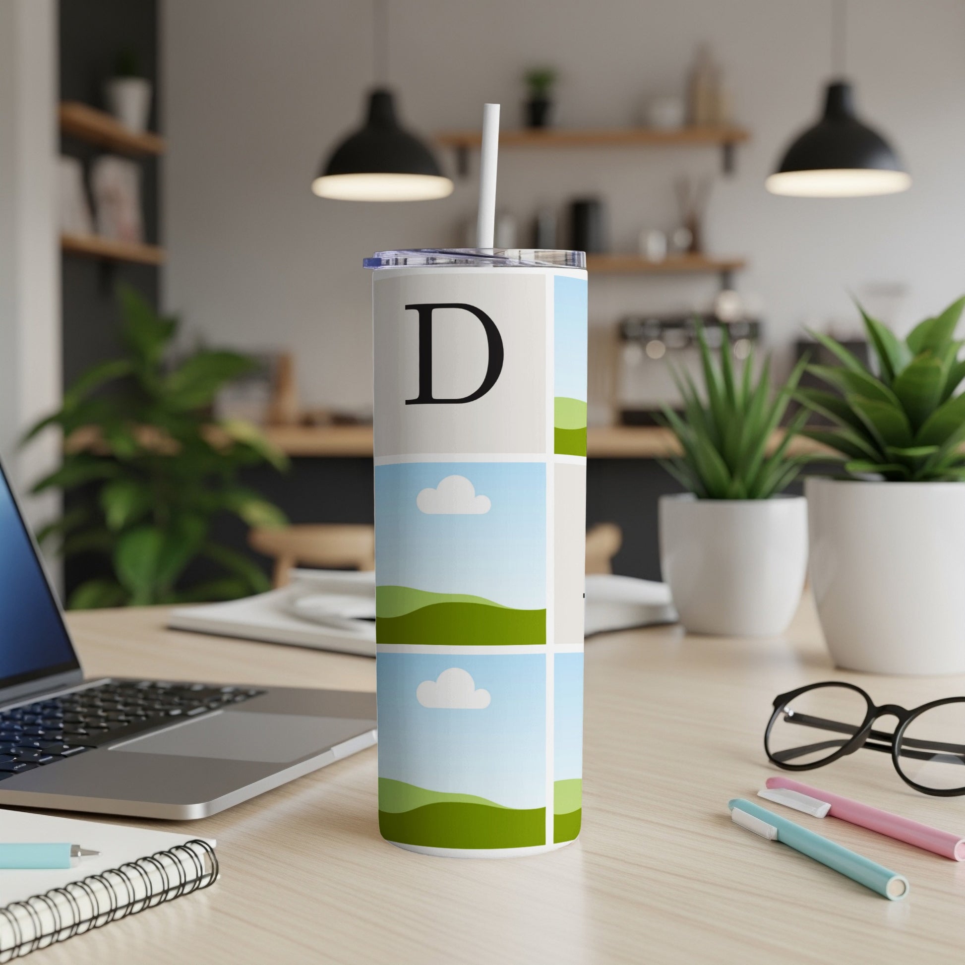 Tumbler with a large letter D and segmented landscape photos on a desk.