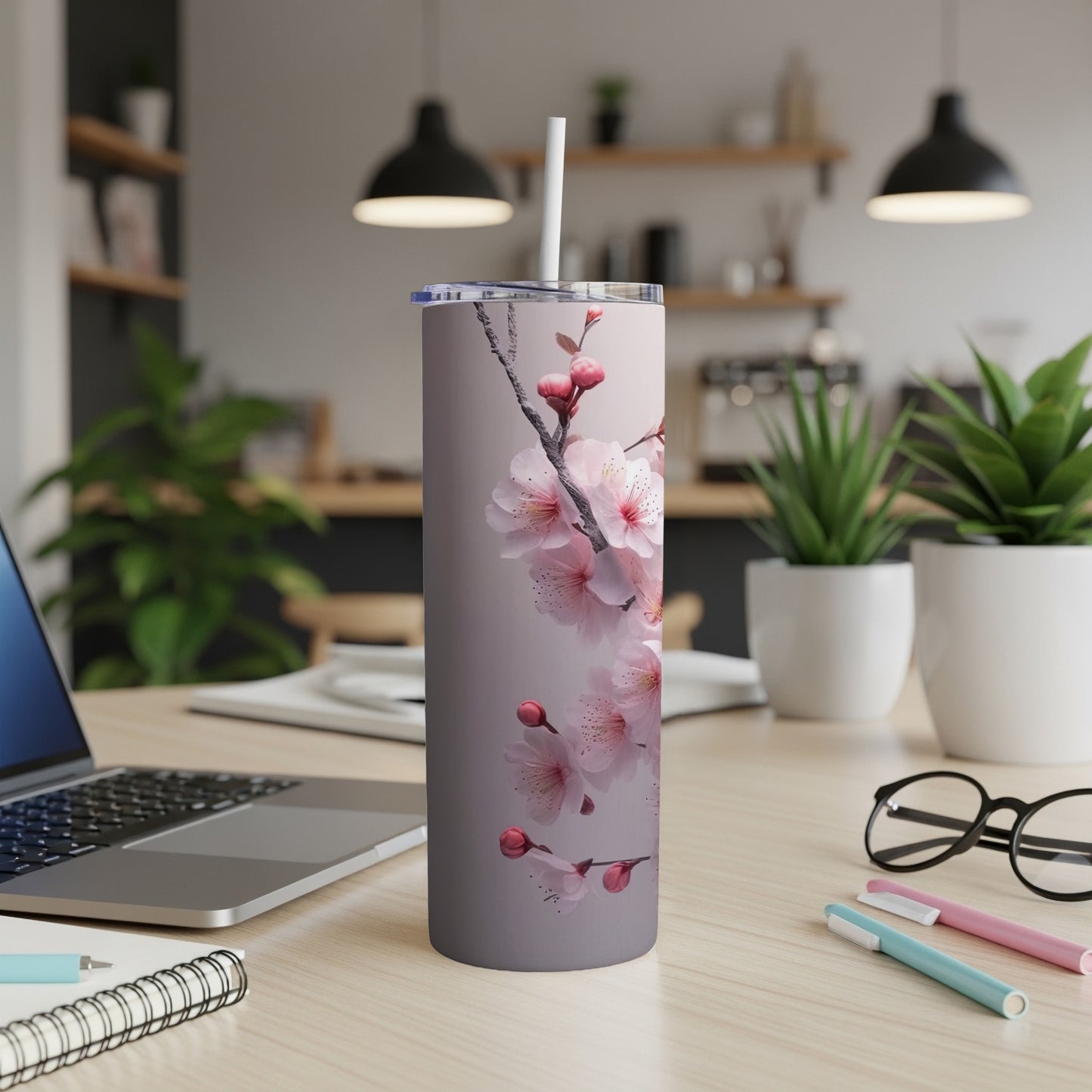 Tall tumbler with pink cherry blossoms and a straw on a desk.