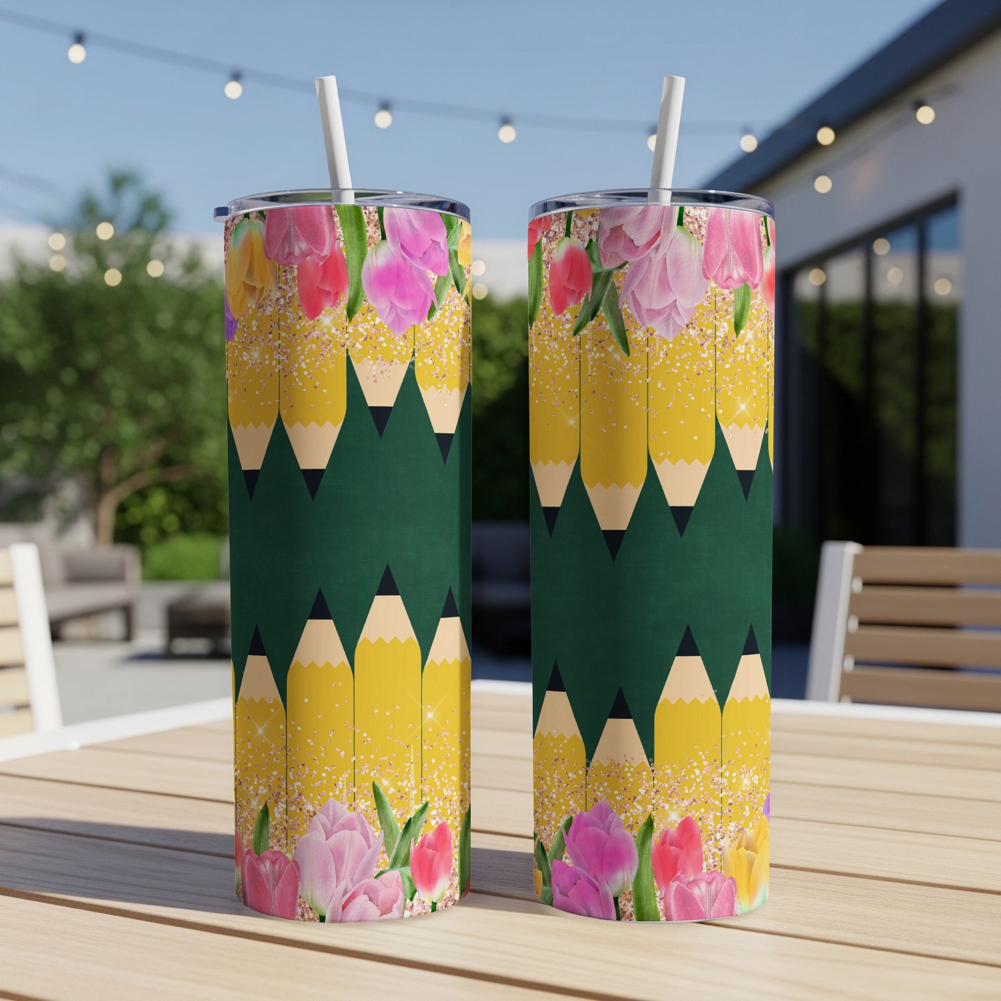 Two tumblers with yellow pencils and pink tulips pattern on outdoor table.