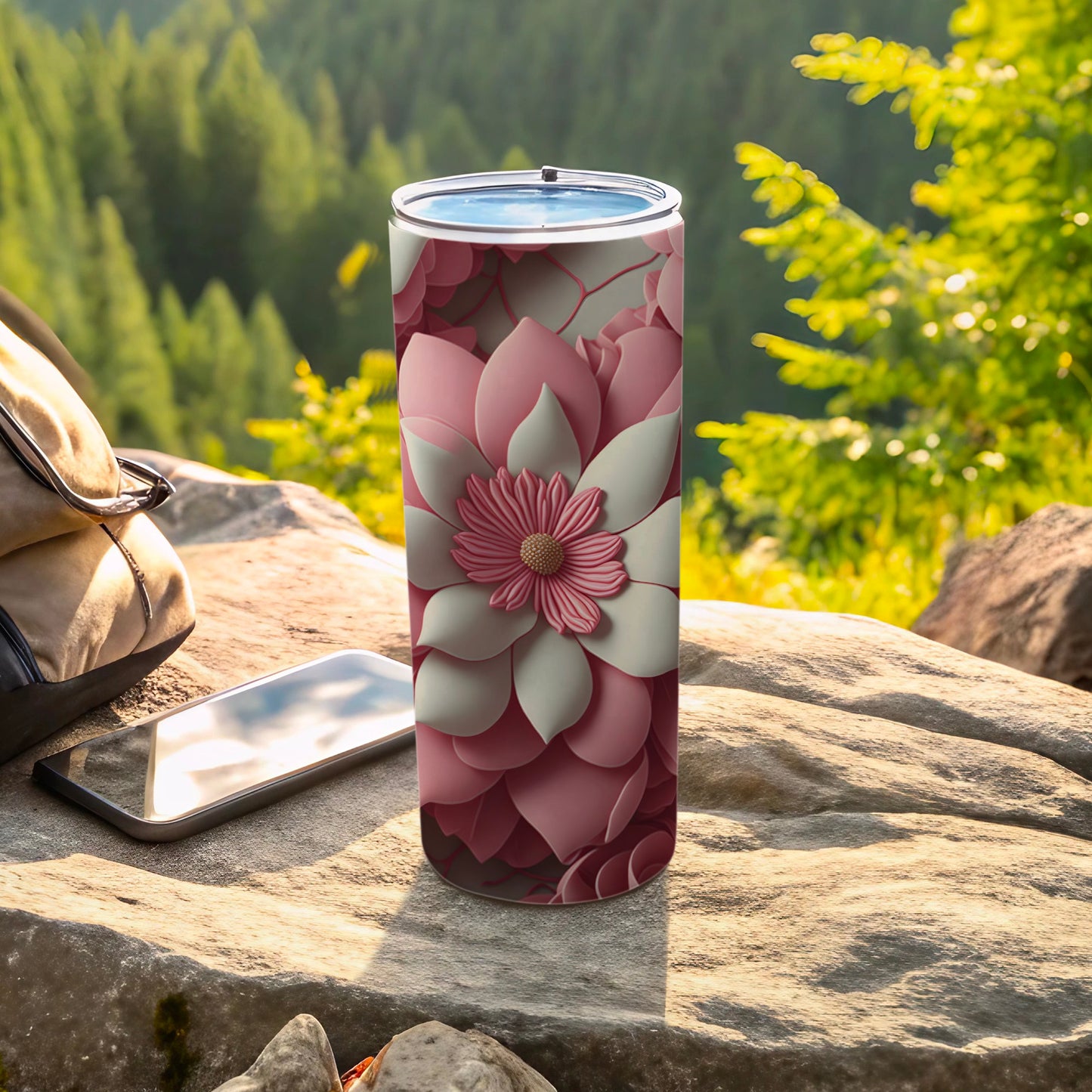 Pink floral tumbler on rock with phone and backpack outdoors.