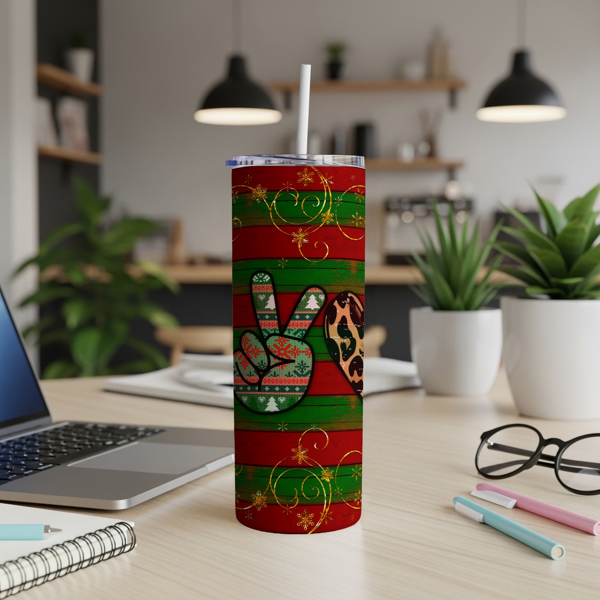 Red and green striped tumbler with peace sign and heart, on a desk.