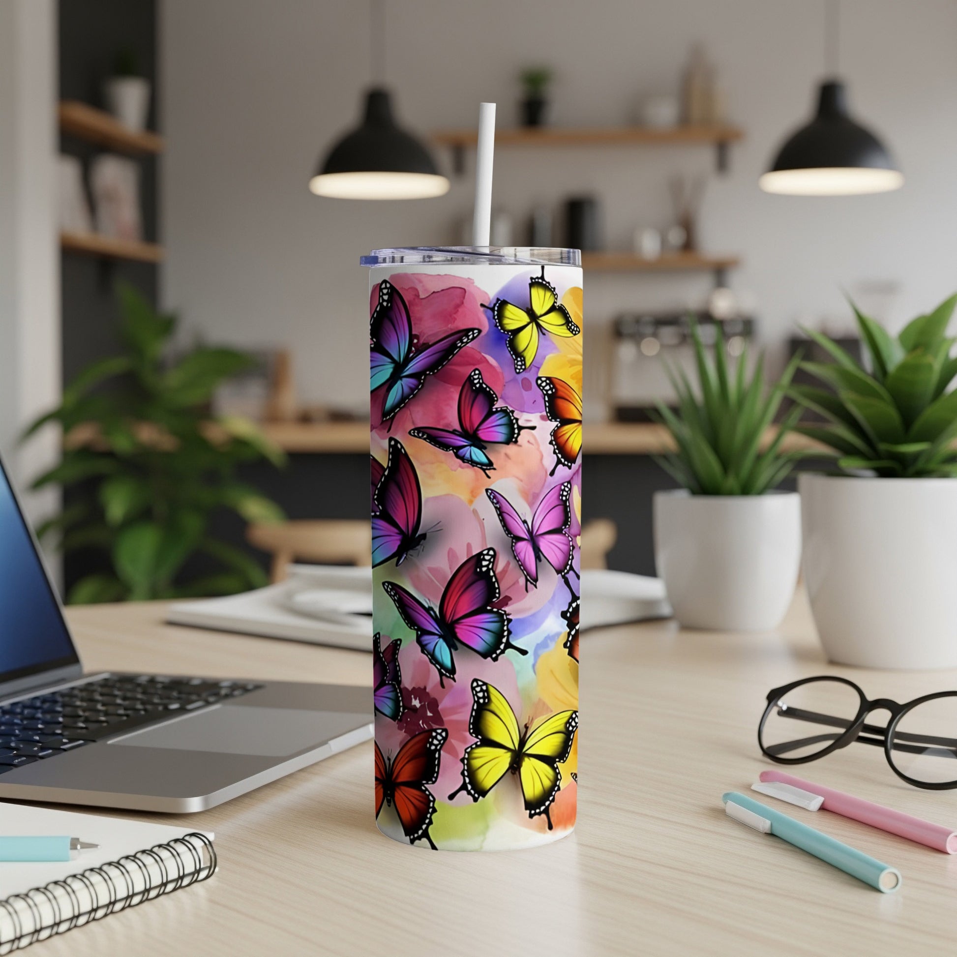 Colorful butterflies adorn a white tumbler on a desk with a laptop and supplies.
