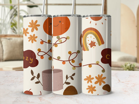 "Cozy" tumbler with autumn-themed illustrations of sun, rainbow, leaves, and candle.