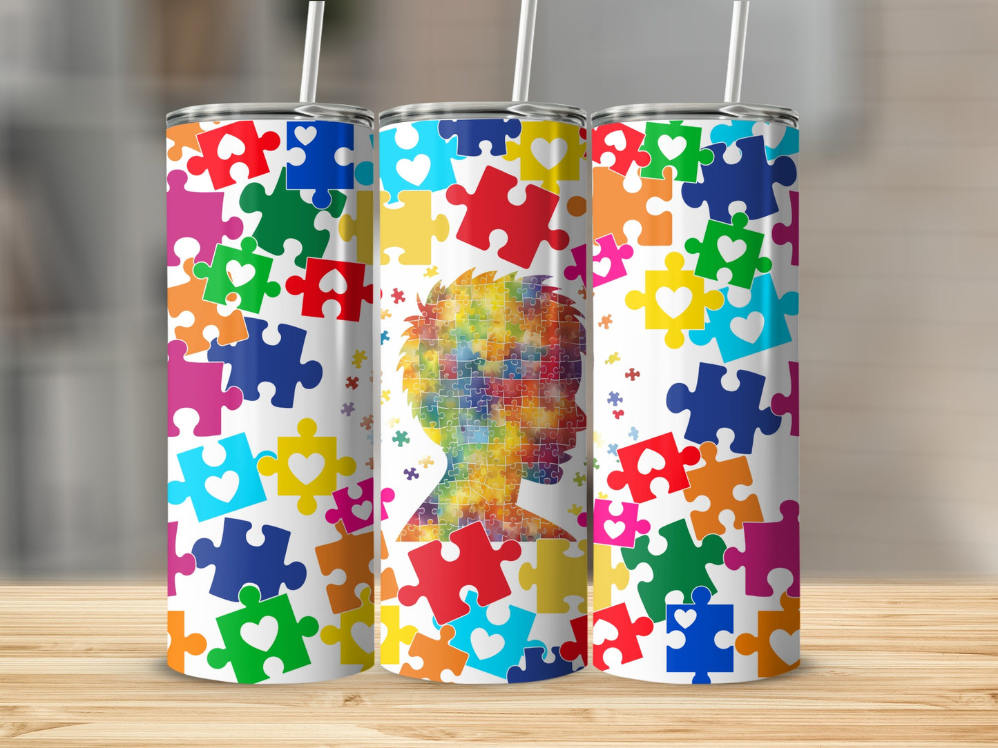 Three tumblers decorated with colorful puzzle pieces and an autism awareness silhouette.