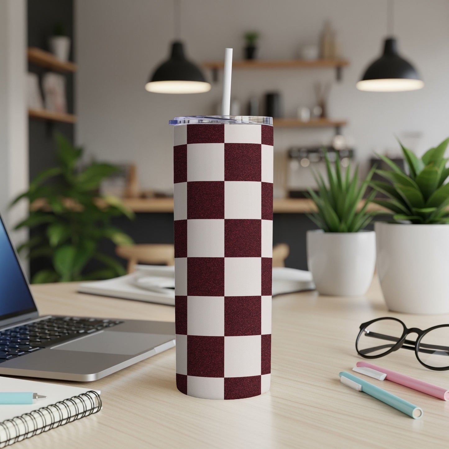 Maroon and white checkered tumbler with straw on a desk.