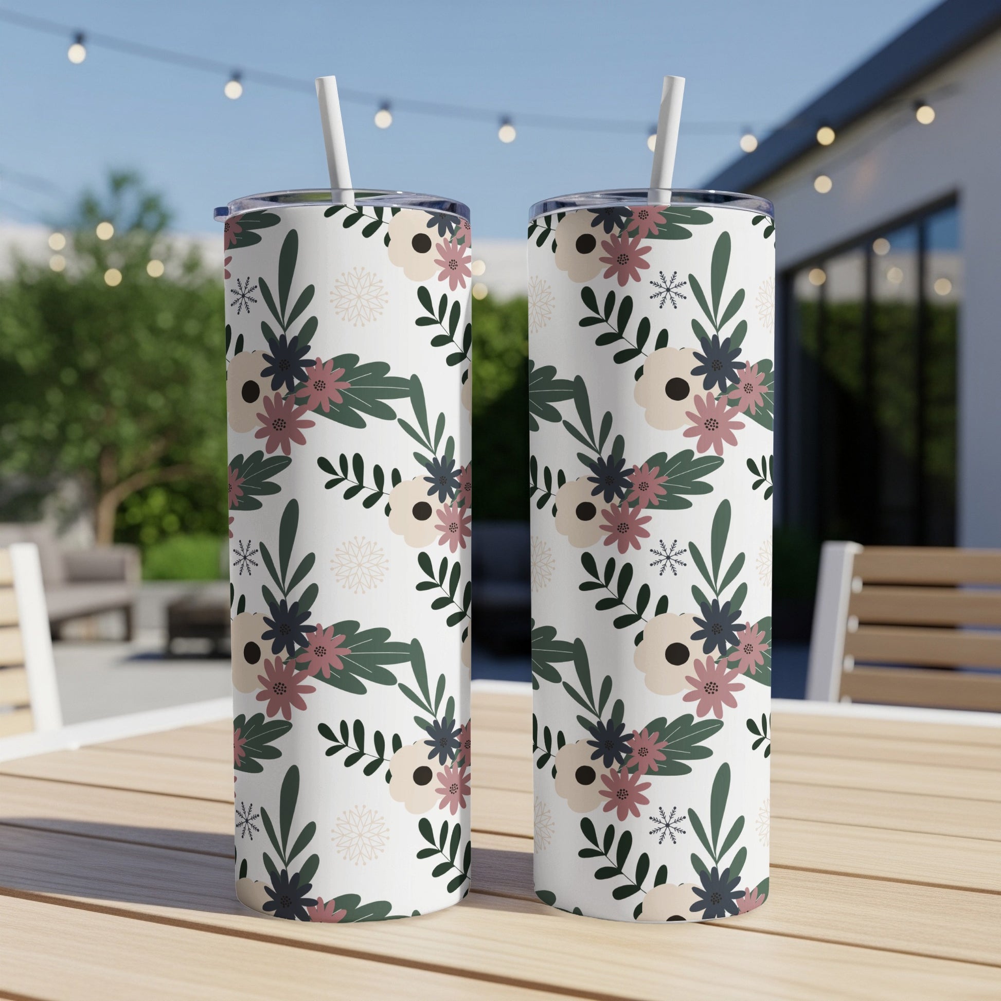 Two white tumblers with a floral pattern sit on a wooden table outdoors.
