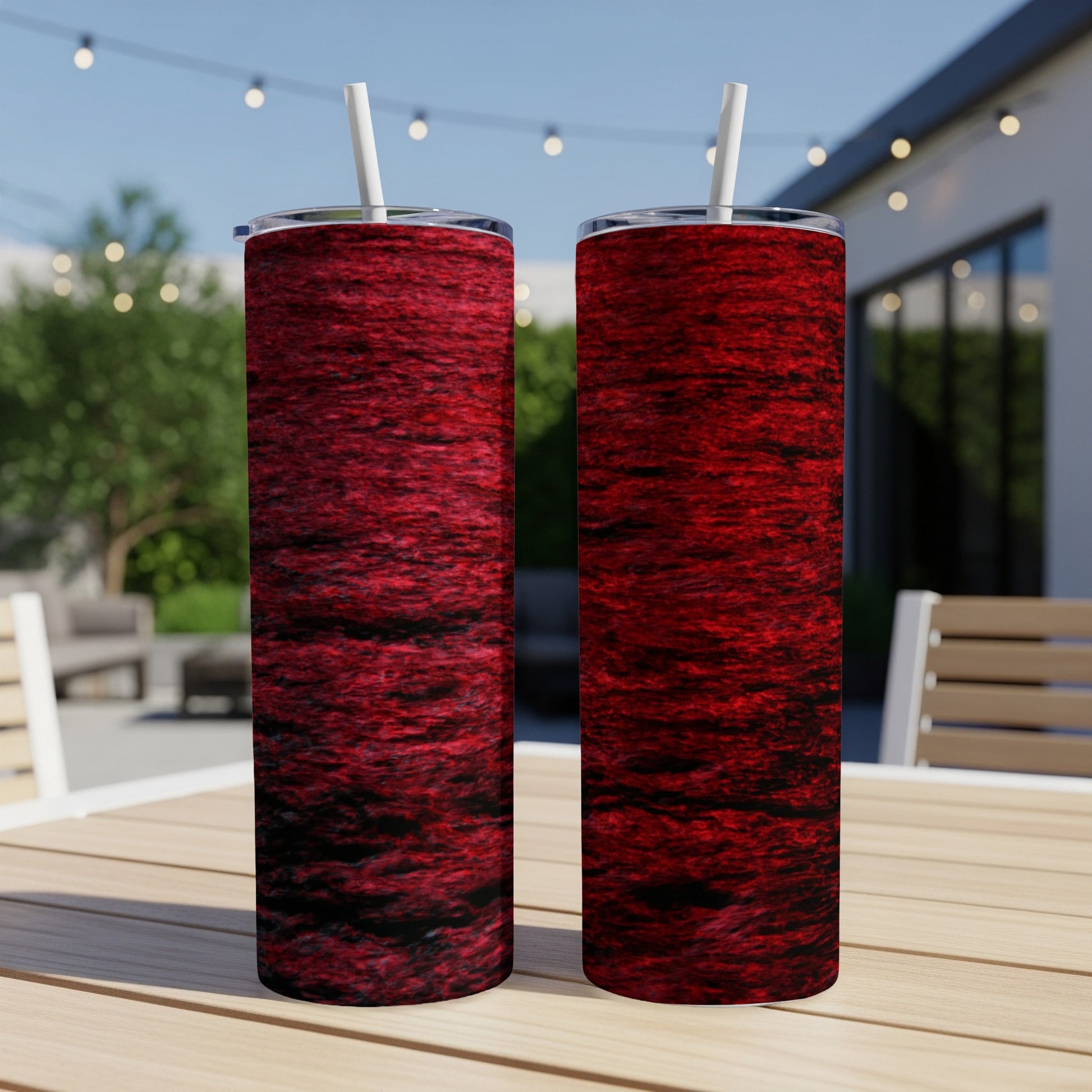 Two red textured tumblers with straws on a wooden table outdoors.