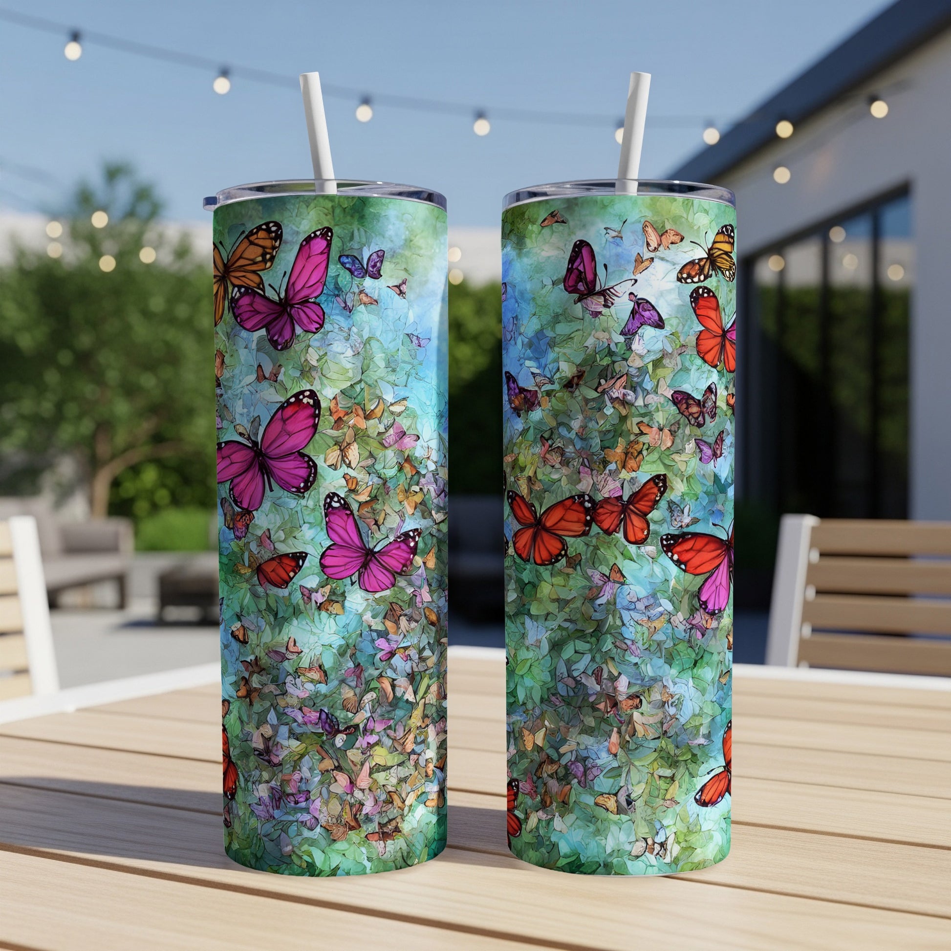 Two tumblers with a colorful butterfly and floral design on an outdoor table.