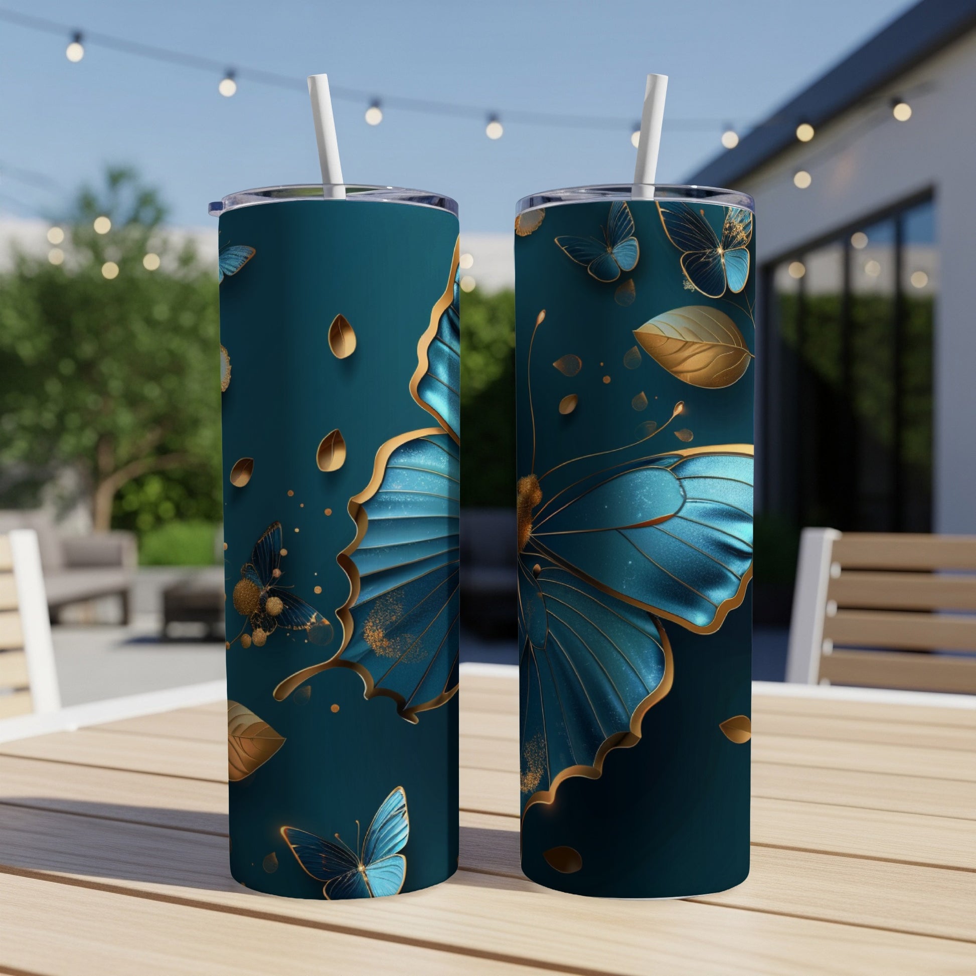 Two teal tumblers with gold butterfly and leaf designs on a wooden table.
