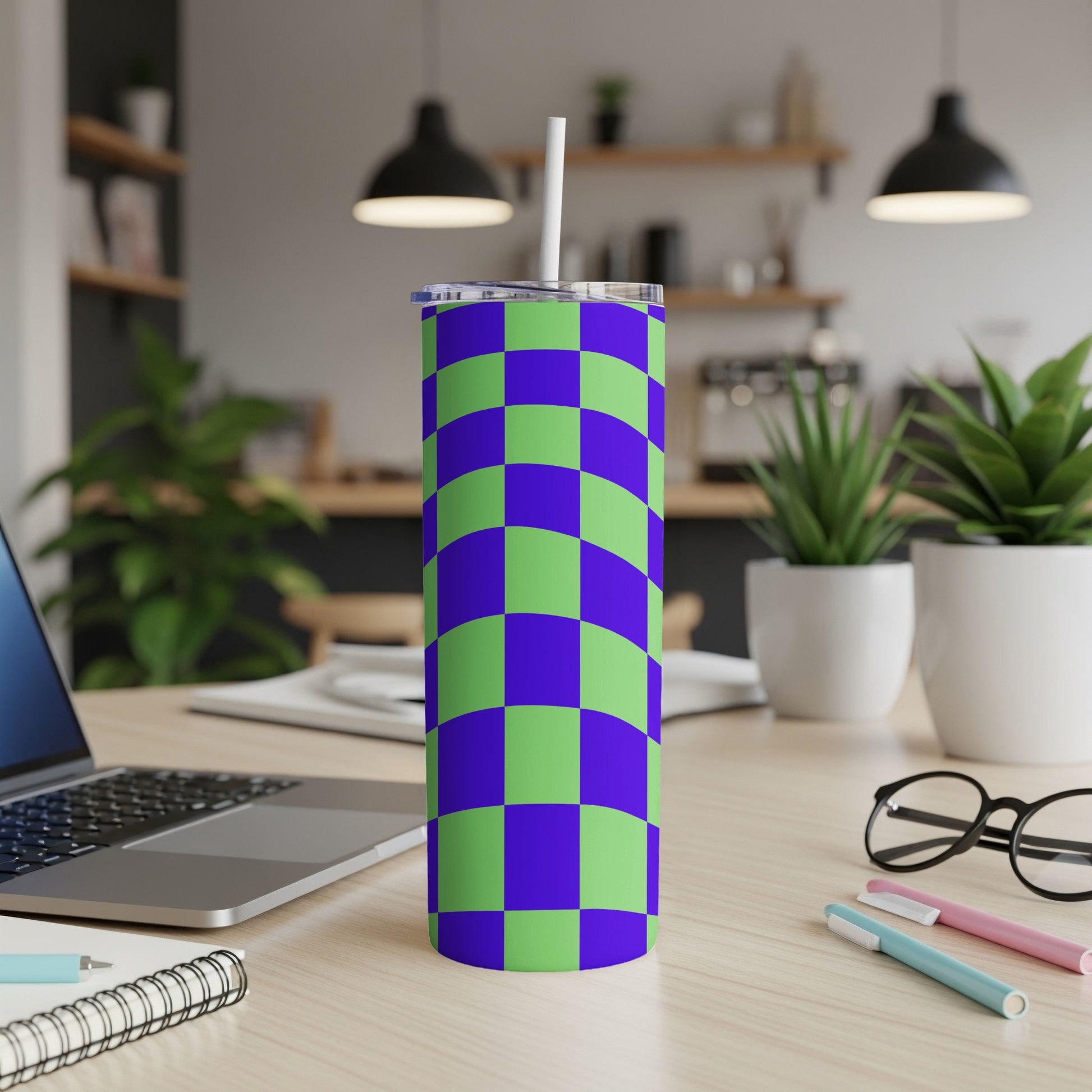 Green and purple checkered tumbler with a straw on a desk.