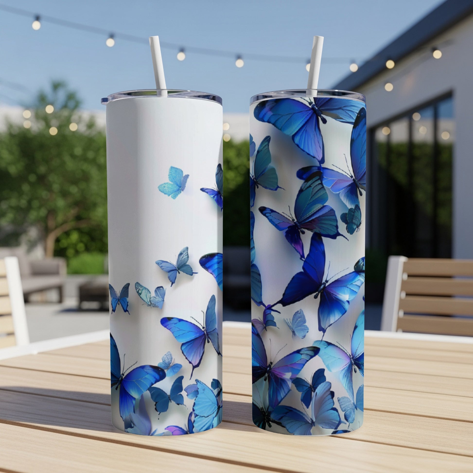 Two white tumblers with blue butterflies and straws on a table.