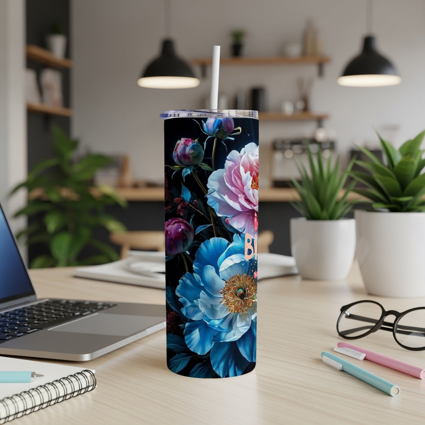Tall tumbler with floral design and straw on a wooden desk.