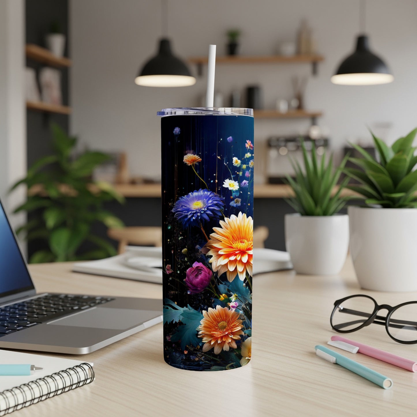 Dark tumbler with vibrant floral design, on a desk with laptop and pens.