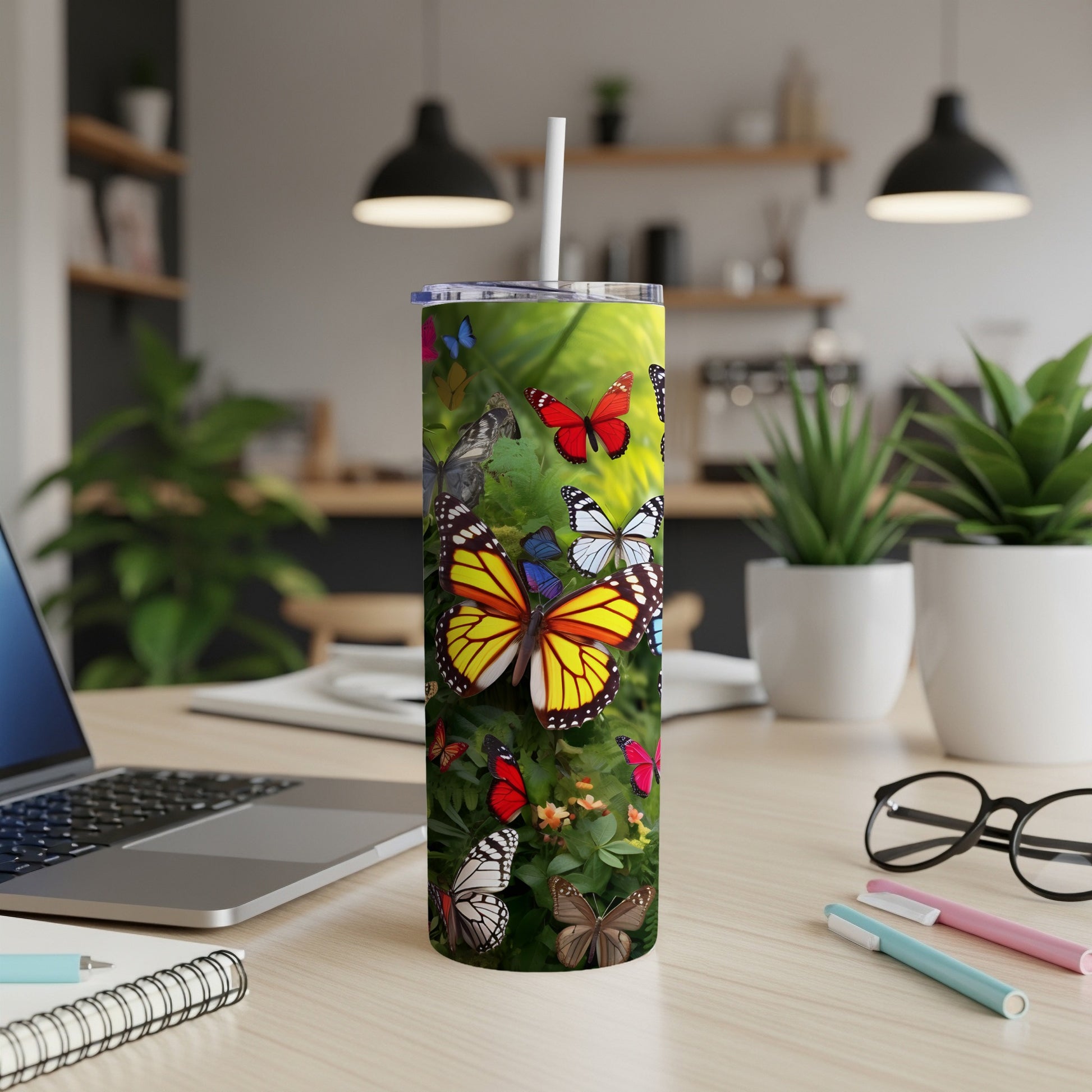 Tall tumbler with colorful butterflies, on a desk with a laptop and pens.