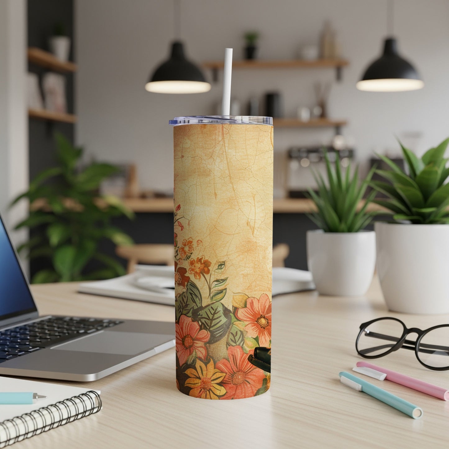 Floral patterned tumbler with a straw on a desk with a laptop and pens.