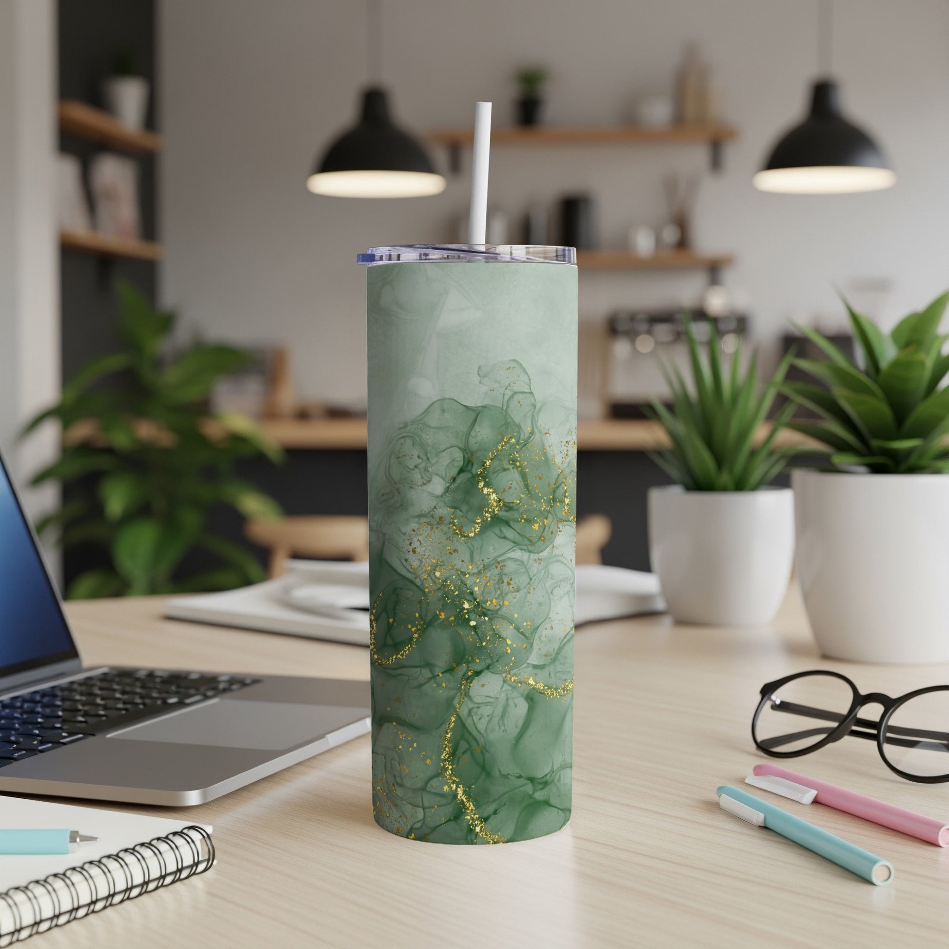 Green marble tumbler with gold glitter accents on a wooden desk.