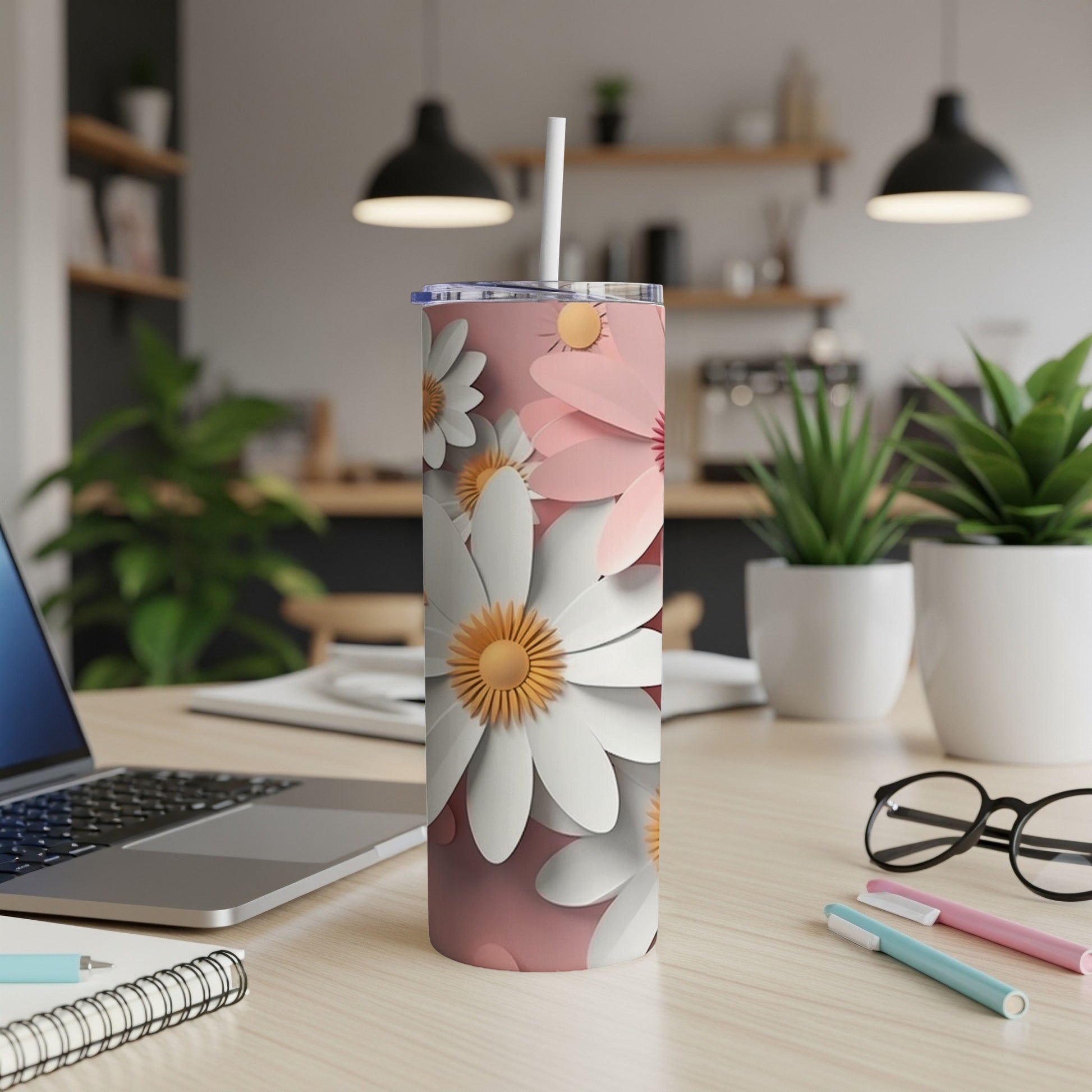 Pink tumbler with white and yellow daisy pattern on a desk.