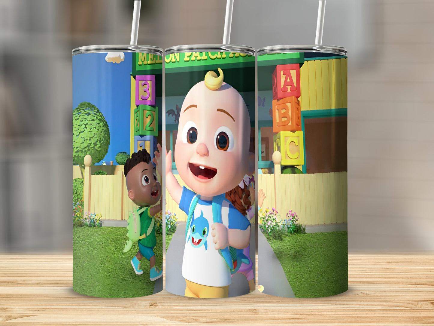 Three tumblers featuring Cocomelon characters and ABC blocks on a wood background.