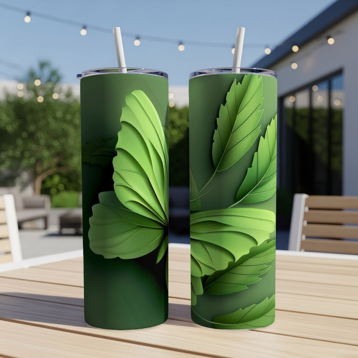 Green tumbler with layered leaf design and straw, on outdoor table.