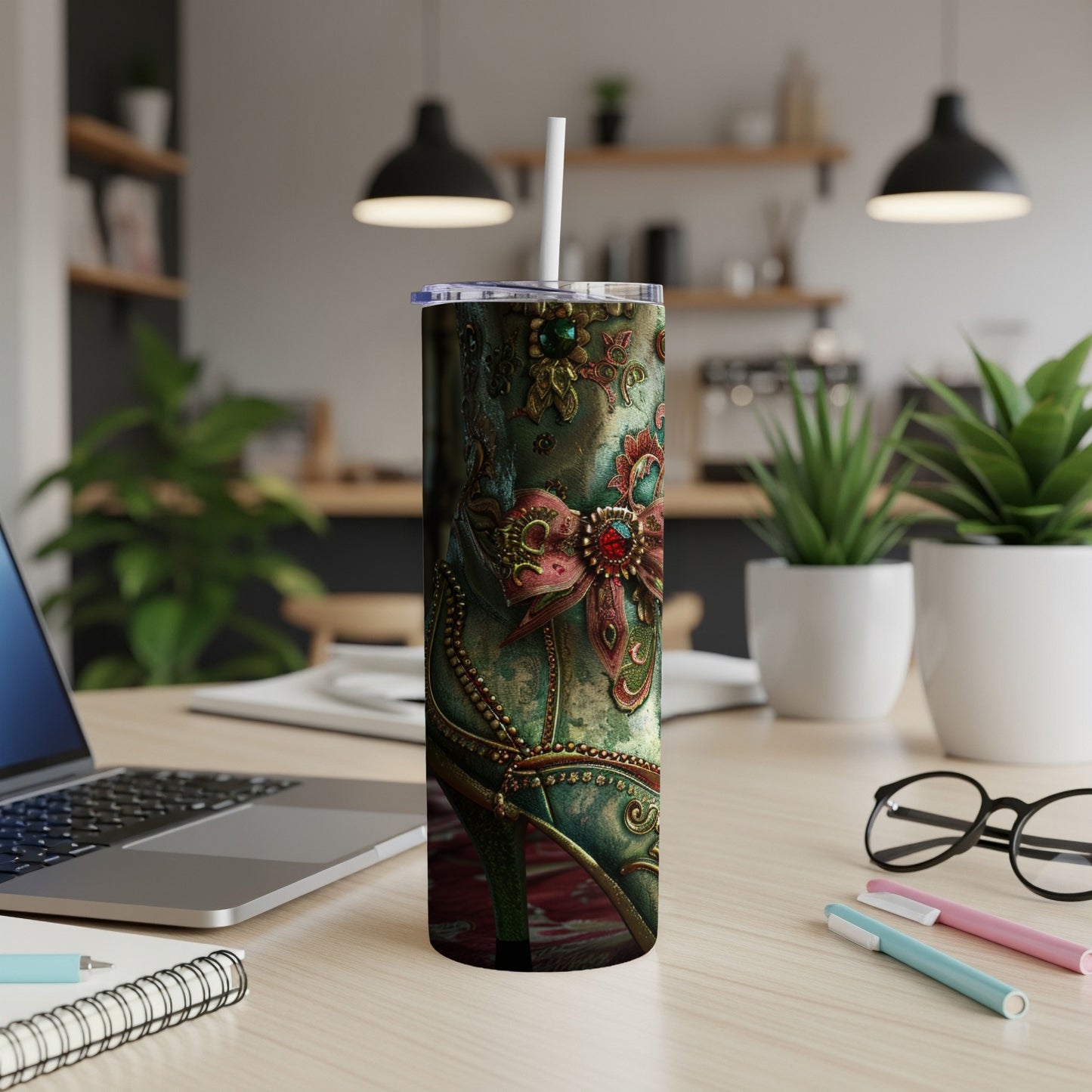 Tall tumbler with ornate, antique-style shoe design, laptop, and office supplies.