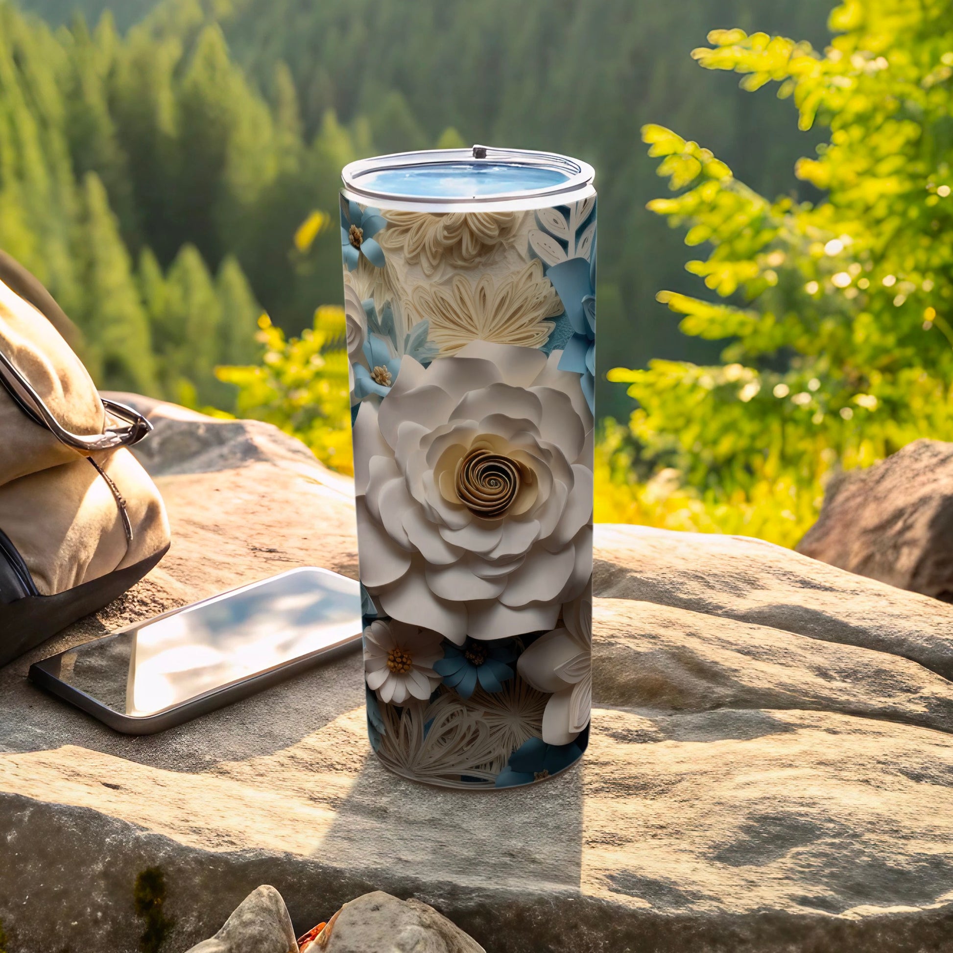 Floral tumbler on a rock with a phone and backpack outdoors.
