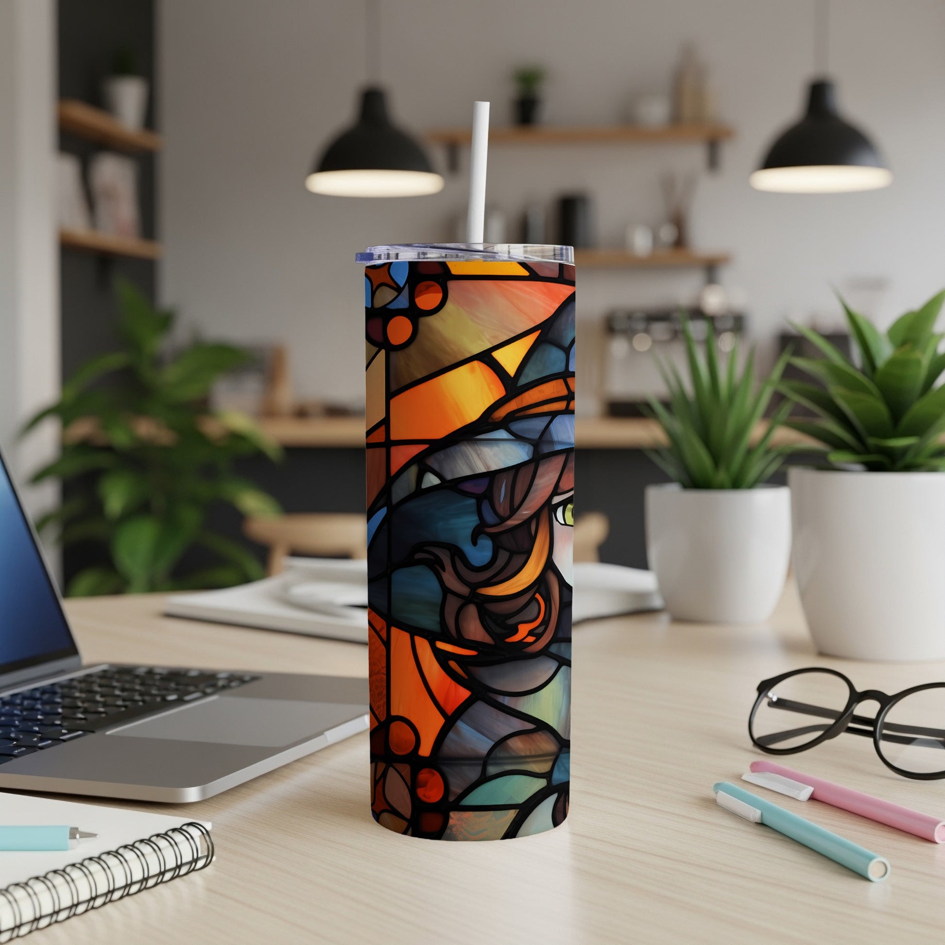 Stained glass style tumbler with witch design and white straw on a desk.