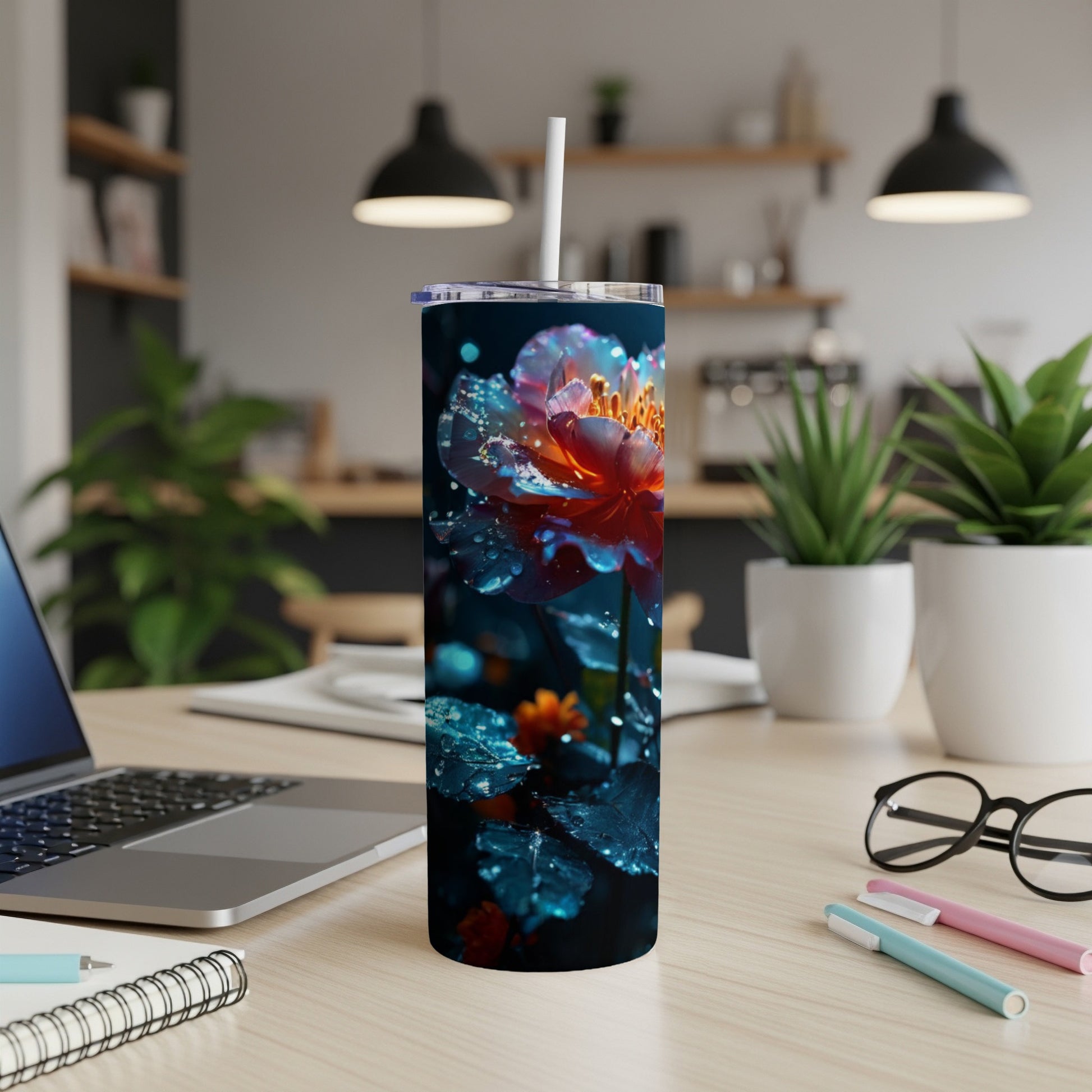 Floral tumbler with straw on a desk beside a laptop and pens.