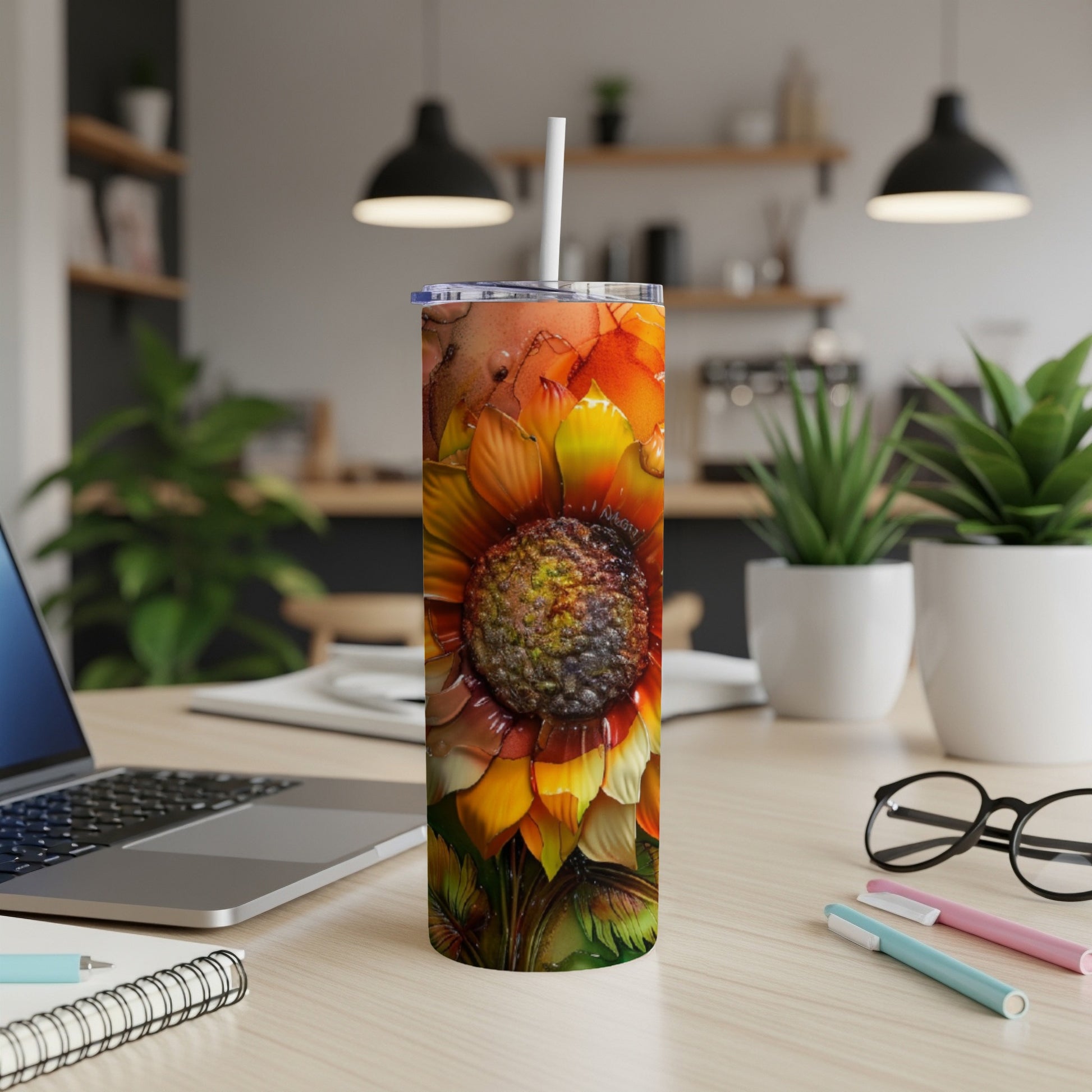 Sunflower tumbler with straw on a desk with laptop and pens.